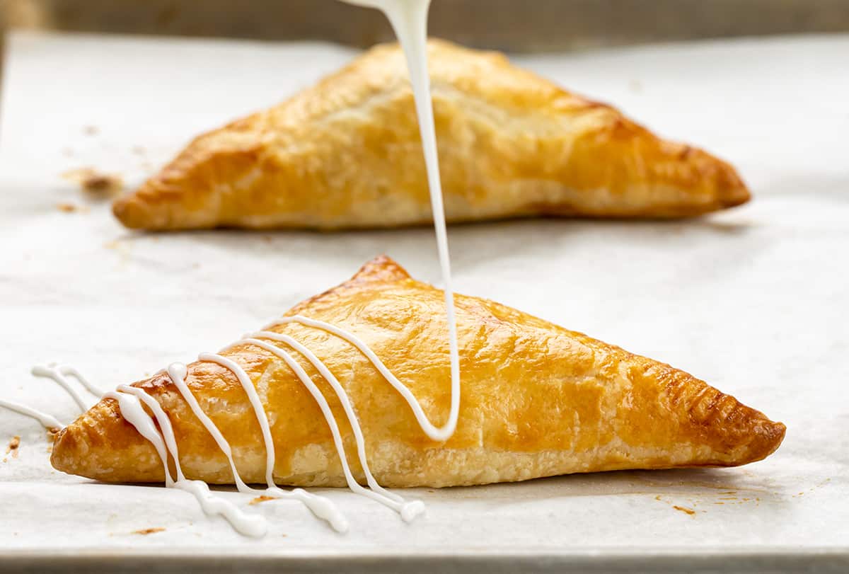 Easy & Amazing Apple Turnovers are filled with spiced apples and baked in flaky, buttery puff pastry dough! Drizzling Glaze Over Baked Apple Turnovers.