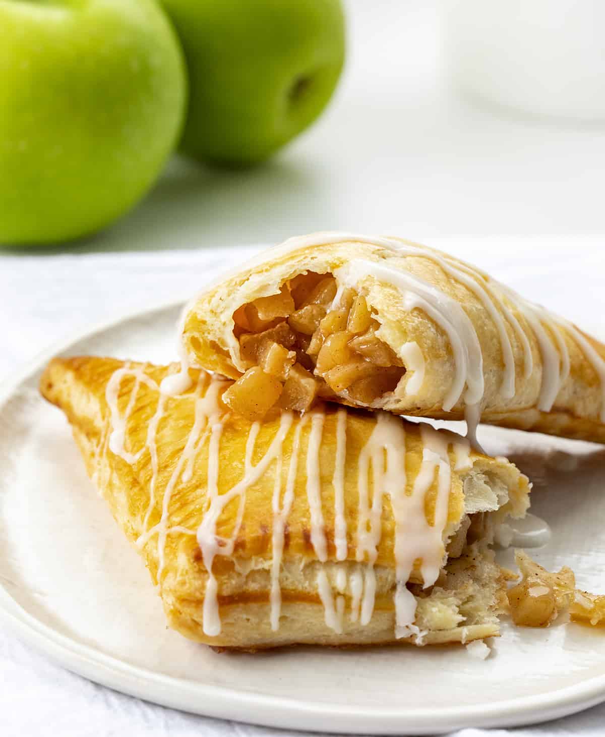 Easy & Amazing Apple Turnovers are filled with spiced apples and baked in flaky, buttery puff pastry dough! Apple Turnovers on a Plate with One Broken in Half and Apple Filling Spilling Out.