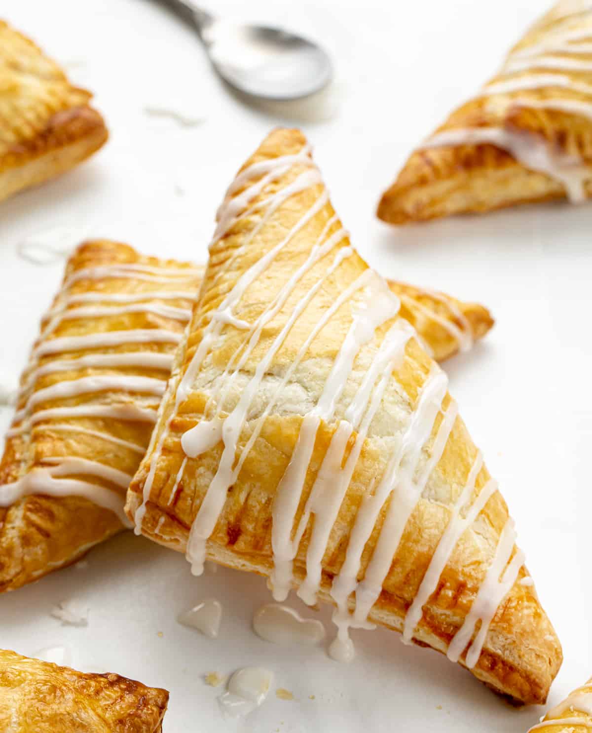 Easy & Amazing Apple Turnovers are filled with spiced apples and baked in flaky, buttery puff pastry dough! Apple Turnovers on a Counter Drizzled in Glaze.
