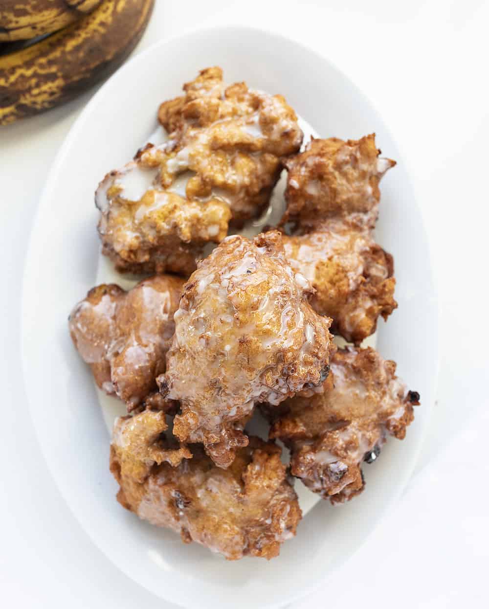 Overhead view of Banana Fritters on a White Plate with Bananas.