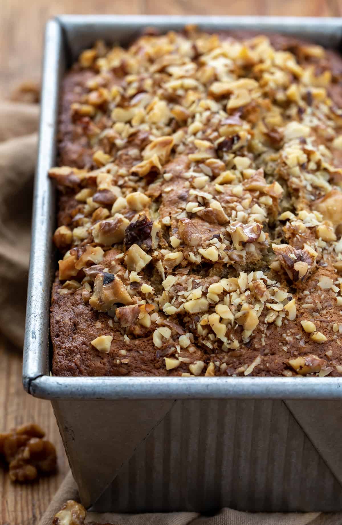 Browned Butter Banana Nut Bread is made by browning butter to add a toasty taste and then loading and topping the bread with chopped walnuts to add even more nutty flavor. It is definitely a step up from traditional banana bread and possibly my new favorite way to enjoy it! (If you prefer a recipe without nuts, I also have my Best Banana Bread Recipe you will want to try.) Close up of Brown Butter Banana Nut Bread in Pan on Butting Board.