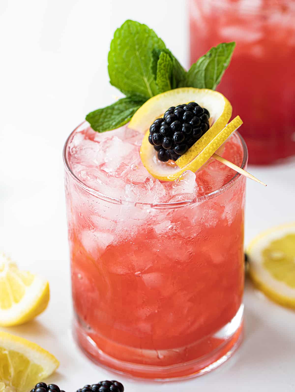 Blackberry Fizz is a refreshing cocktail made with blackberries, freshly squeezed lemon juice, vodka, simple syrup, and club soda. It's just like a blackberry bramble but without blackberry liqueur. It offers a delightful combination of fruity, tangy, and refreshing flavors, making it a perfect choice for a summer sip or any time you're in the mood for a vibrant and lively beverage! Blackberry Fizz Cocktails on a White Counter with Blackberry Lemon Garnish.