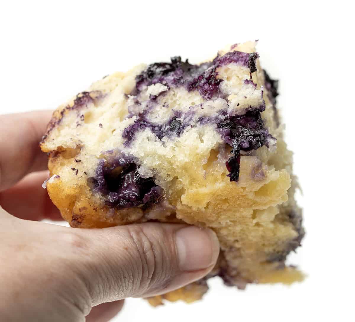 Blueberry Butter Swim Biscuits combine the flavors of blueberries, butter, and a hint of sweetness with a moist and fluffy crumb and crispy golden brown top. They can be enjoyed as a breakfast treat, a snack, or even as a dessert! Plus, they are SO EASY to make! Hand Holding Blueberry Butter Swim Biscuit and Showing the Bottom Soaked in Butter.