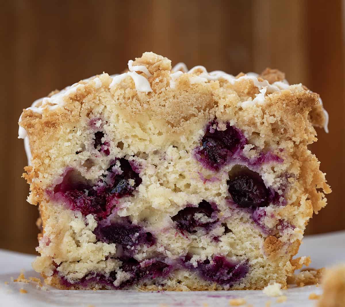 Blueberry Lemon Loaf is a moist cake-like loaf loaded with fresh blueberries and lemon flavor, topped and baked with a crumble topping. Then, the loaf is drizzled with a sweet glaze to make this a perfect breakfast, snack, or dessert. This is a copycat of the viral Costco Blueberry Lemon Loaf and dare I say, even BETTER!! Loaf of Blueberry Lemon Bread Close up on a Cutting Board with Pieces Removed so The Inside Texture is Showing.