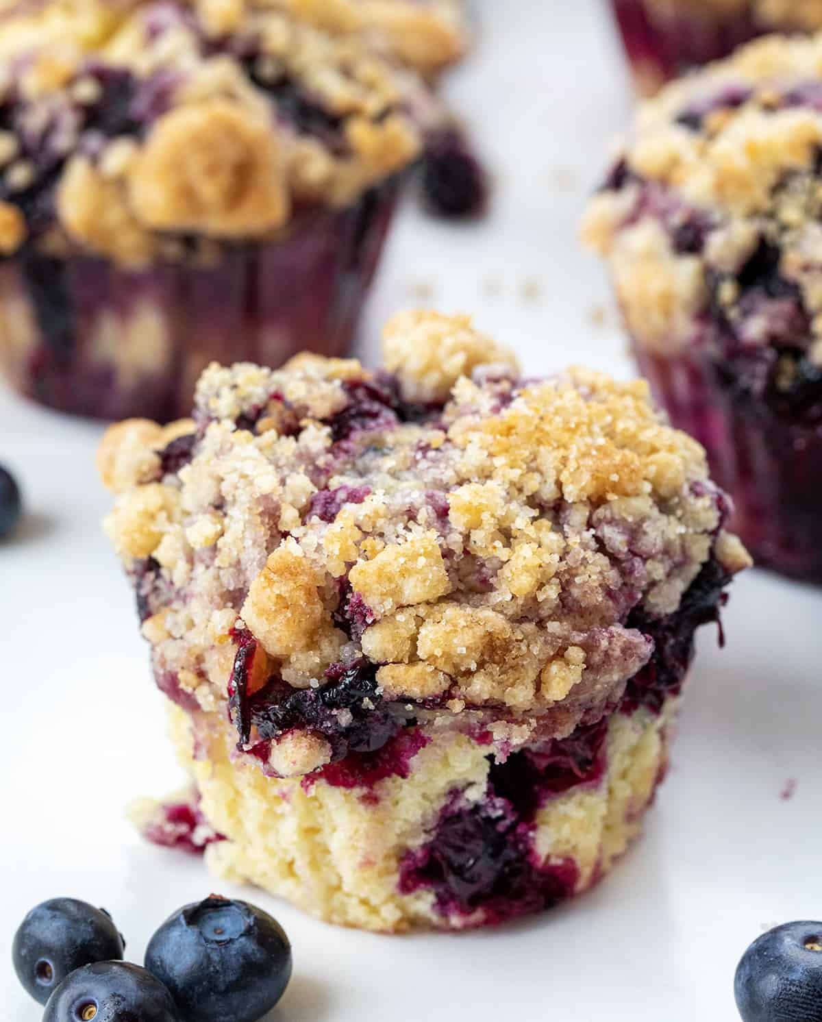 Blueberry Muffins are sweet and fluffy muffins made with fresh blueberries, homemade blueberry syrup, and a crumble topping. Double the blueberry! They are a delicious breakfast, snack, or treat to enjoy with a cup of coffee or tea and a great way to use up ripe blueberries! Close up of a Blueberry Muffin.