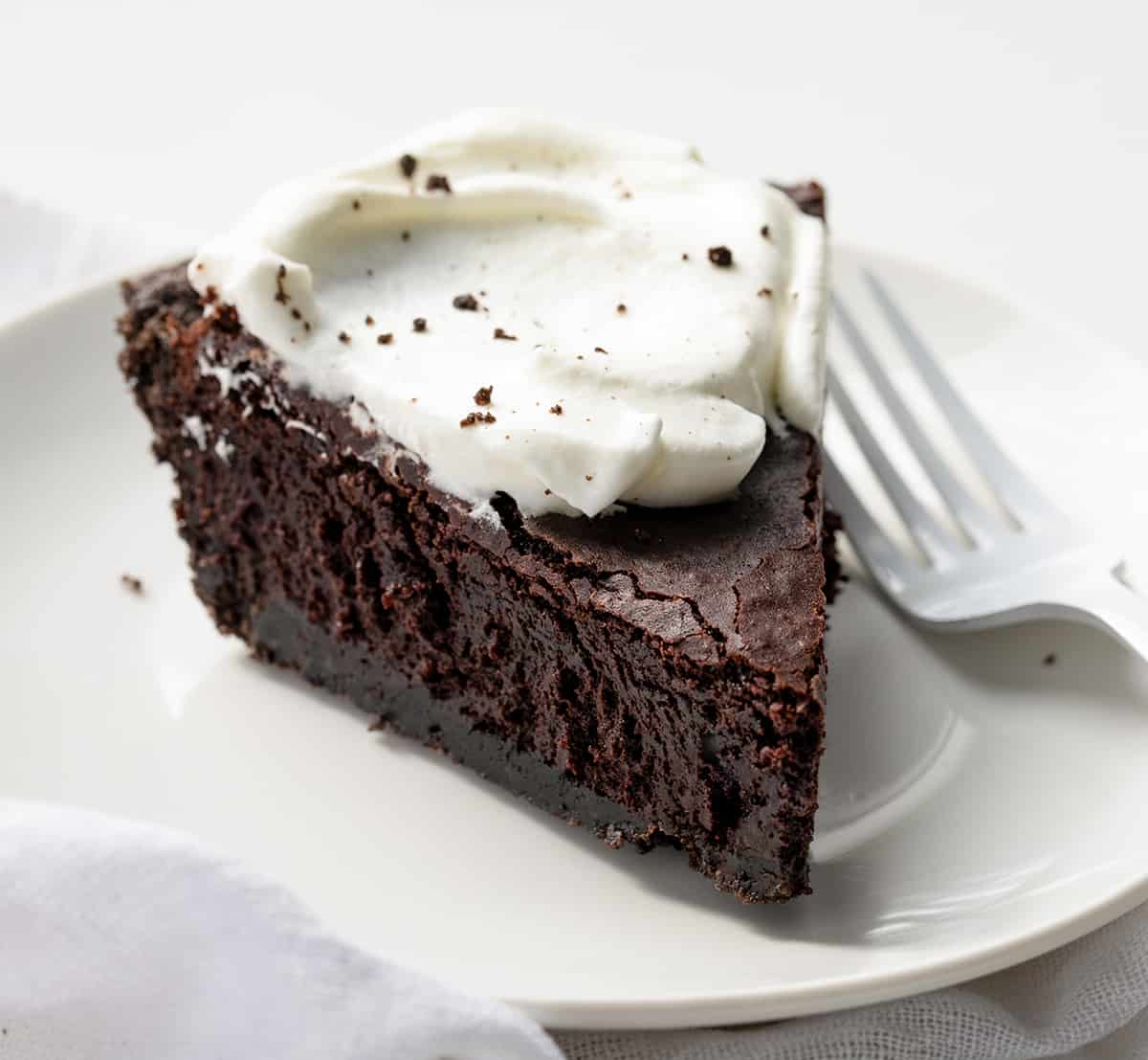Brownie Pie combines the irresistible textures of a crisp Oreo cookie crust, dense and fudgy brownies, and fluffy whipped cream with a chocolate drizzle. It's a perfect dessert for special occasions or anytime you're craving a truly indulgent treat! Piece of Brownie Pie on a White Plate with Whipped Cream.