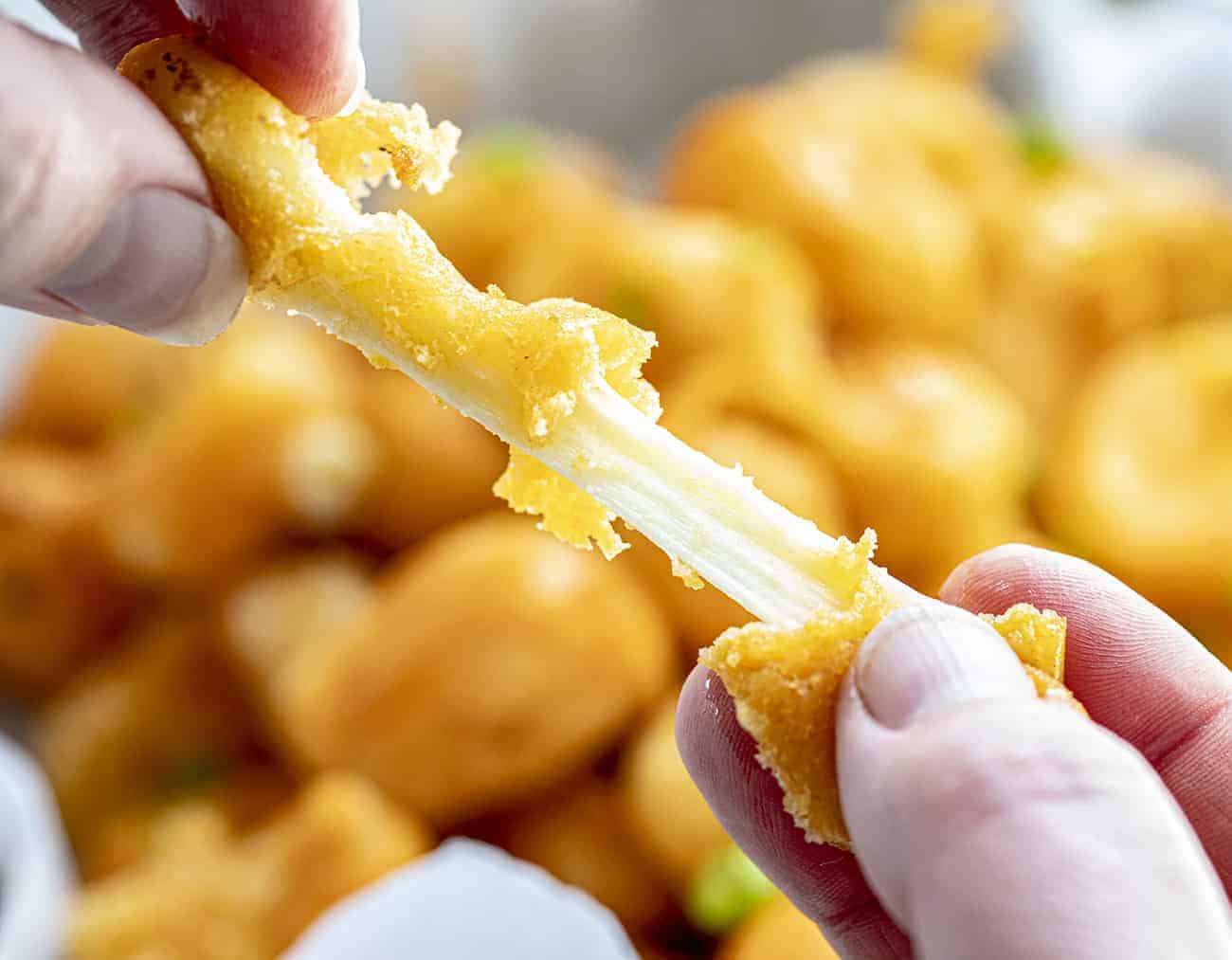 Buffalo Cheese Curds are cheese curds that are breaded in a buffalo-flavored batter using my homemade buffalo sauce and fried to a crisp golden brown. buffalo cheese curds, cheese curds, deep-fried cheese curds, fried cheese curds, white cheddar cheese curds, state fair foods, appetizers, iambaker, i am baker, homemade cheese curds Pulling Apart a Buffalo Cheese Curd with Two Hands