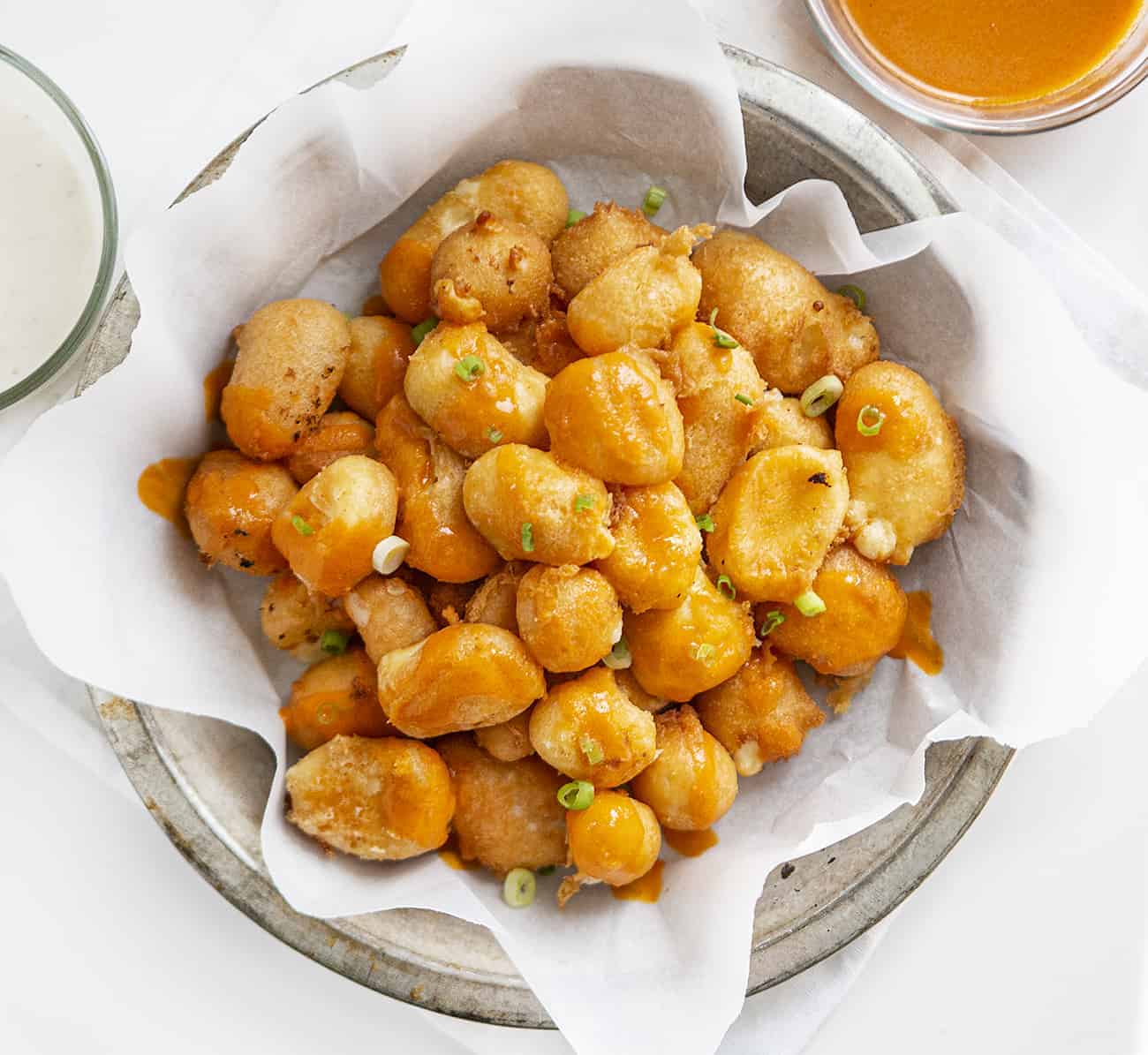 Buffalo Cheese Curds are cheese curds that are breaded in a buffalo-flavored batter using my homemade buffalo sauce and fried to a crisp golden brown. buffalo cheese curds, cheese curds, deep-fried cheese curds, fried cheese curds, white cheddar cheese curds, state fair foods, appetizers, iambaker, i am baker, homemade cheese curds Overhead view of plate with Buffalo Cheese Curds in it and Buffalo Sauce and Ranch on the Side