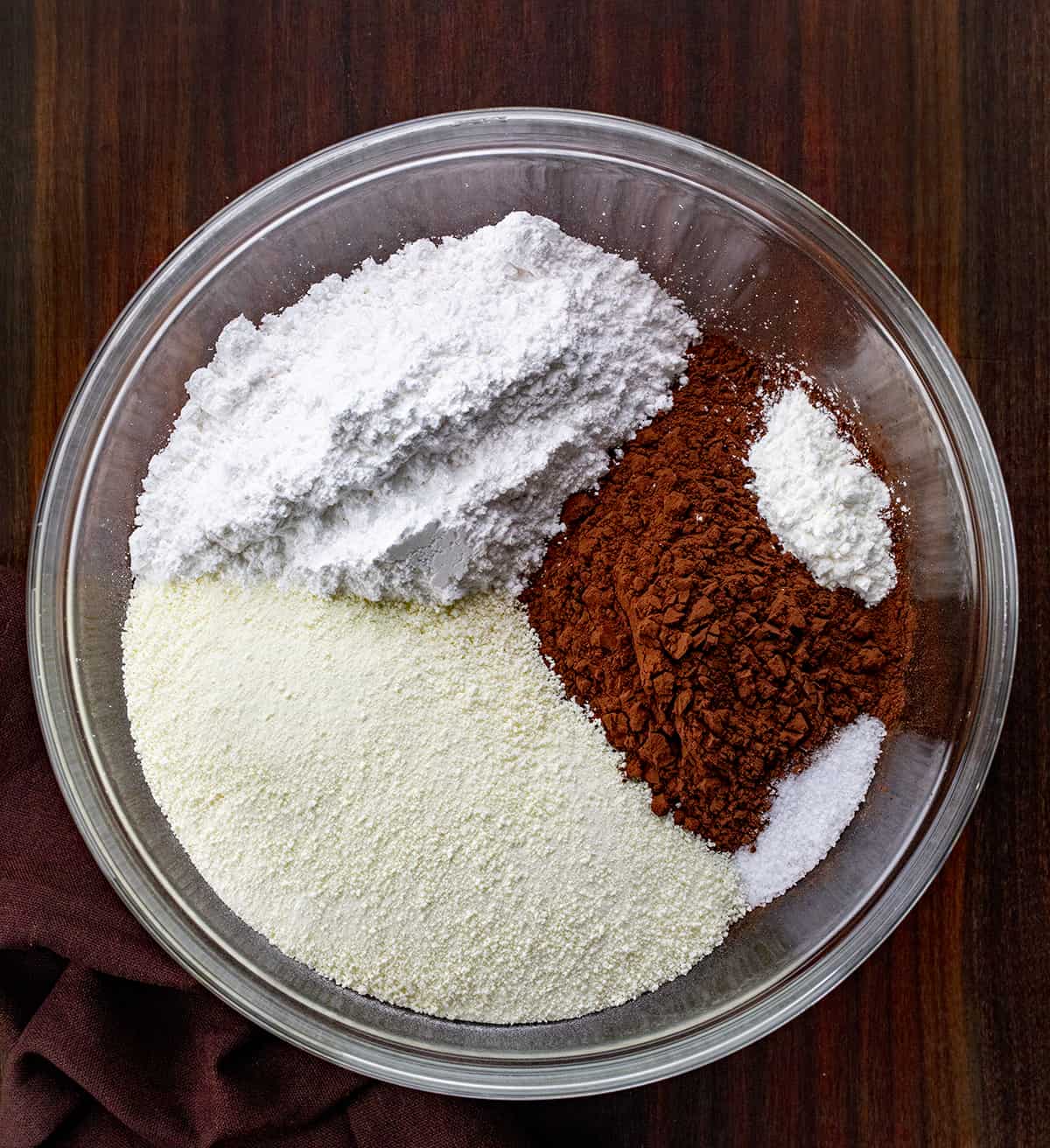 Homemade Hot Cocoa Mix is cheaper than store-bought and tastes so much better! Nothing warms a body up like a mug of rich hot cocoa, especially in the winter. And, it's a beverage that can be enjoyed by all ages. I love that you know exactly what is going into the powdery mix with no added preservatives. This hot chocolate recipe is rich, velvety, decadent, and the perfect beverage for a crowd! Ingredients for making homemade hot cocoa mix in a bowl on a cutting board.