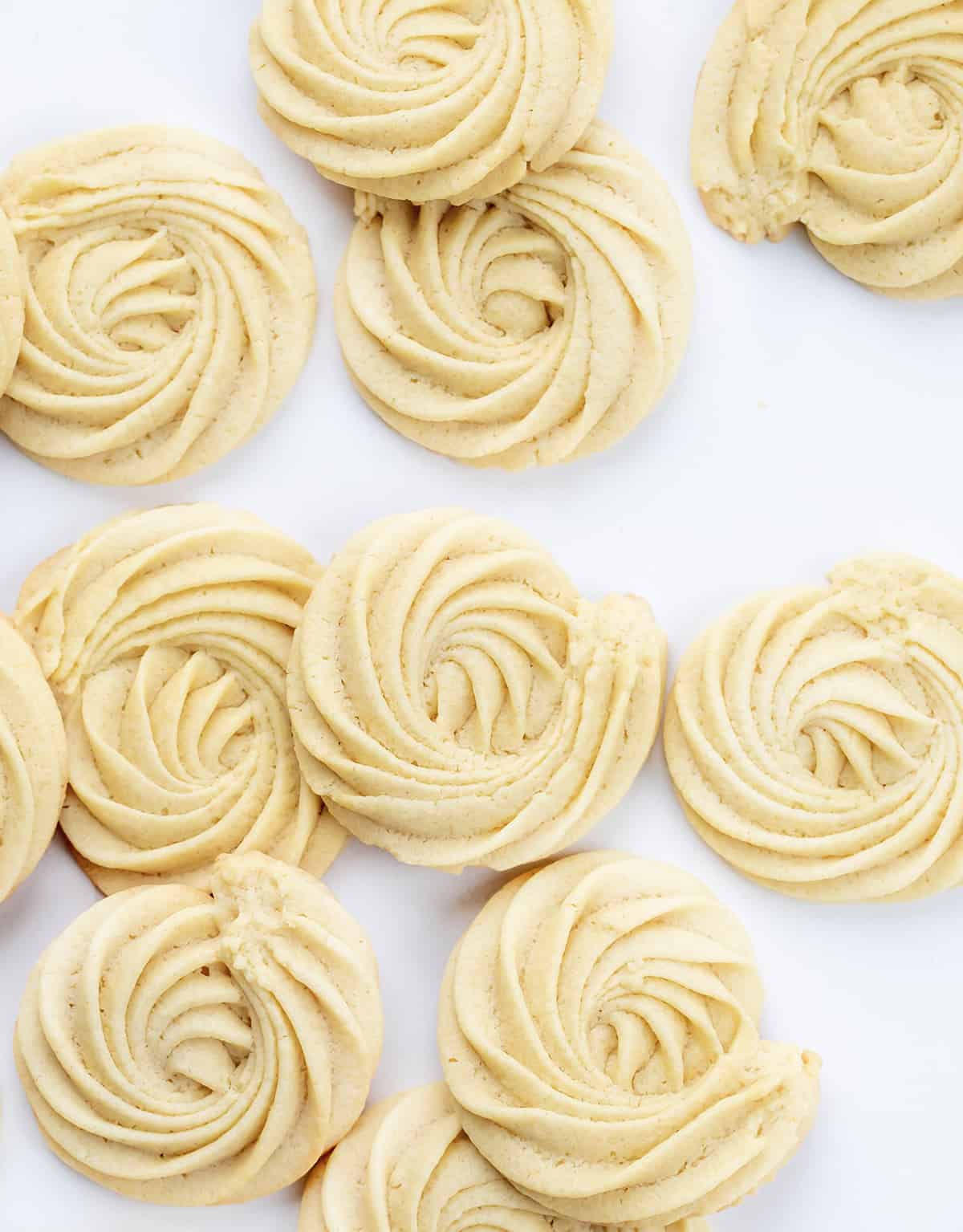Butter Cookies are buttery, tender cookies that can be enjoyed as-is with a cup of coffee or tea or as a base for decorating holiday cookies. They are synonymous with Christmas cookies (remember the blue tin?), and I wanted to find a recipe as easy as possible. I know how busy the holiday season can be, so a cookie recipe that does not take all day with no chilling time works for me (and it will for you)! Perfect for a cookie exchange or a Christmas dessert charcuterie board! Many Butter Cookies on a White Counter.
