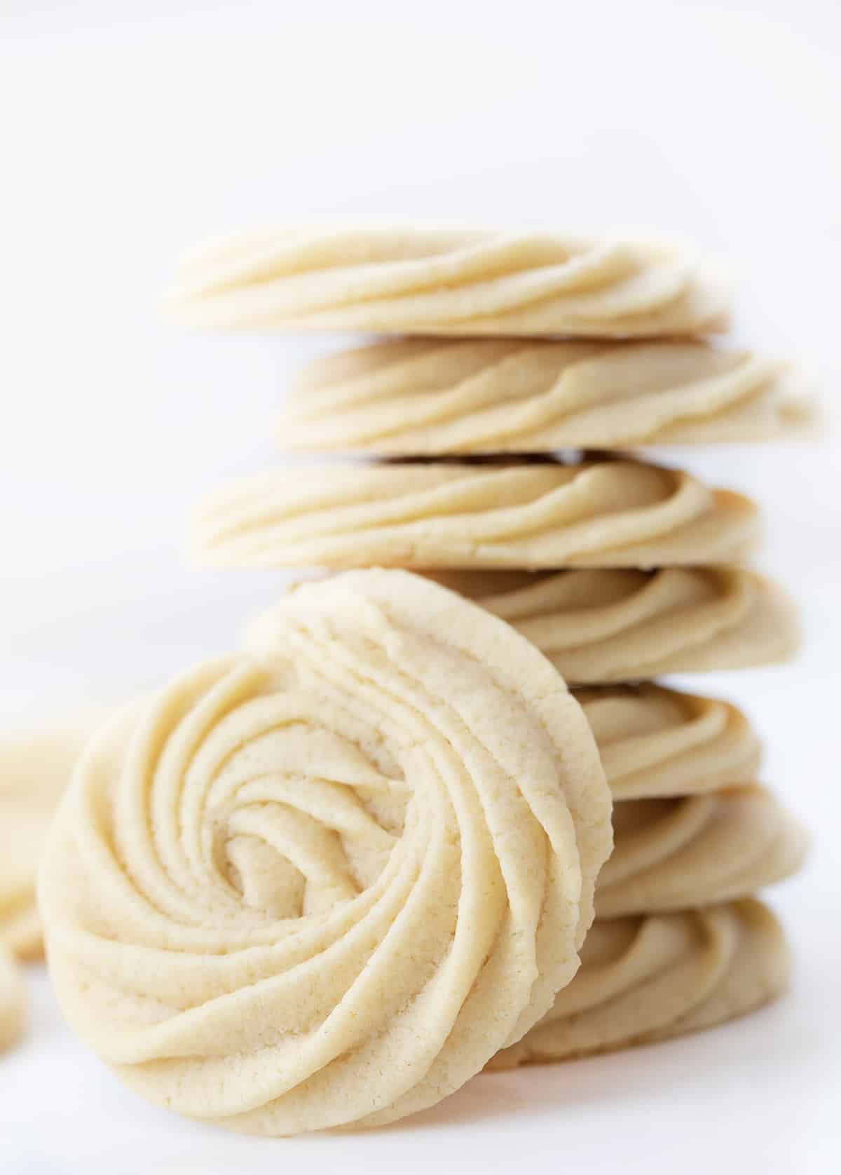 Butter Cookies are buttery, tender cookies that can be enjoyed as-is with a cup of coffee or tea or as a base for decorating holiday cookies. They are synonymous with Christmas cookies (remember the blue tin?), and I wanted to find a recipe as easy as possible. I know how busy the holiday season can be, so a cookie recipe that does not take all day with no chilling time works for me (and it will for you)! Perfect for a cookie exchange or a Christmas dessert charcuterie board! A Stack of Butter Cookies with One Facing the Camera and Close So Details Can be Seen.