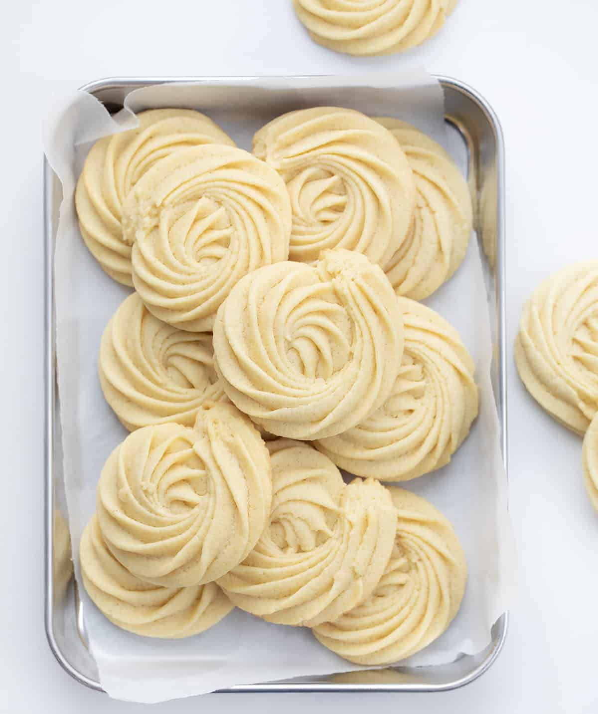 Butter Cookies are buttery, tender cookies that can be enjoyed as-is with a cup of coffee or tea or as a base for decorating holiday cookies. They are synonymous with Christmas cookies (remember the blue tin?), and I wanted to find a recipe as easy as possible. I know how busy the holiday season can be, so a cookie recipe that does not take all day with no chilling time works for me (and it will for you)! Perfect for a cookie exchange or a Christmas dessert charcuterie board! Tray of Butter Cookies on a Counter with Some Cookies off to the Side.