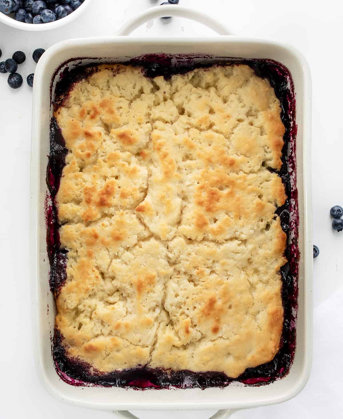 Butter Swim Biscuit Blueberry Cobbler is a delightful dessert that combines homemade blueberry filling with tender, buttery biscuits. It's a perfect treat for gatherings, family meals, or anytime you crave a comforting and fruity dessert. It is so easy to throw together and ready in 30 minutes! Pan of Butter Swim Biscuit Blueberry Cobbler with Fresh Blueberries.