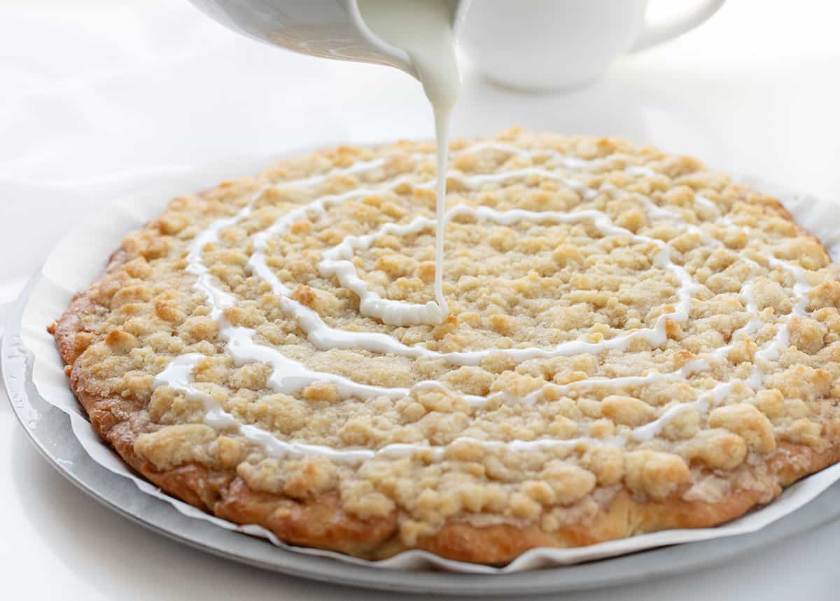 Cactus Bread is a sweet, soft, slightly spiced dessert pizza that folks who go to Pizza Ranch restaurant make a special point to get! The actual Pizza Ranch recipe is a closely guarded secret, but I think this version is just as delicious! It starts with a light and airy focaccia crust topped with cinnamon butter and a delightful crumble topping that will leave everyone craving more! Drizzling Glaze Over Dessert Pizza.