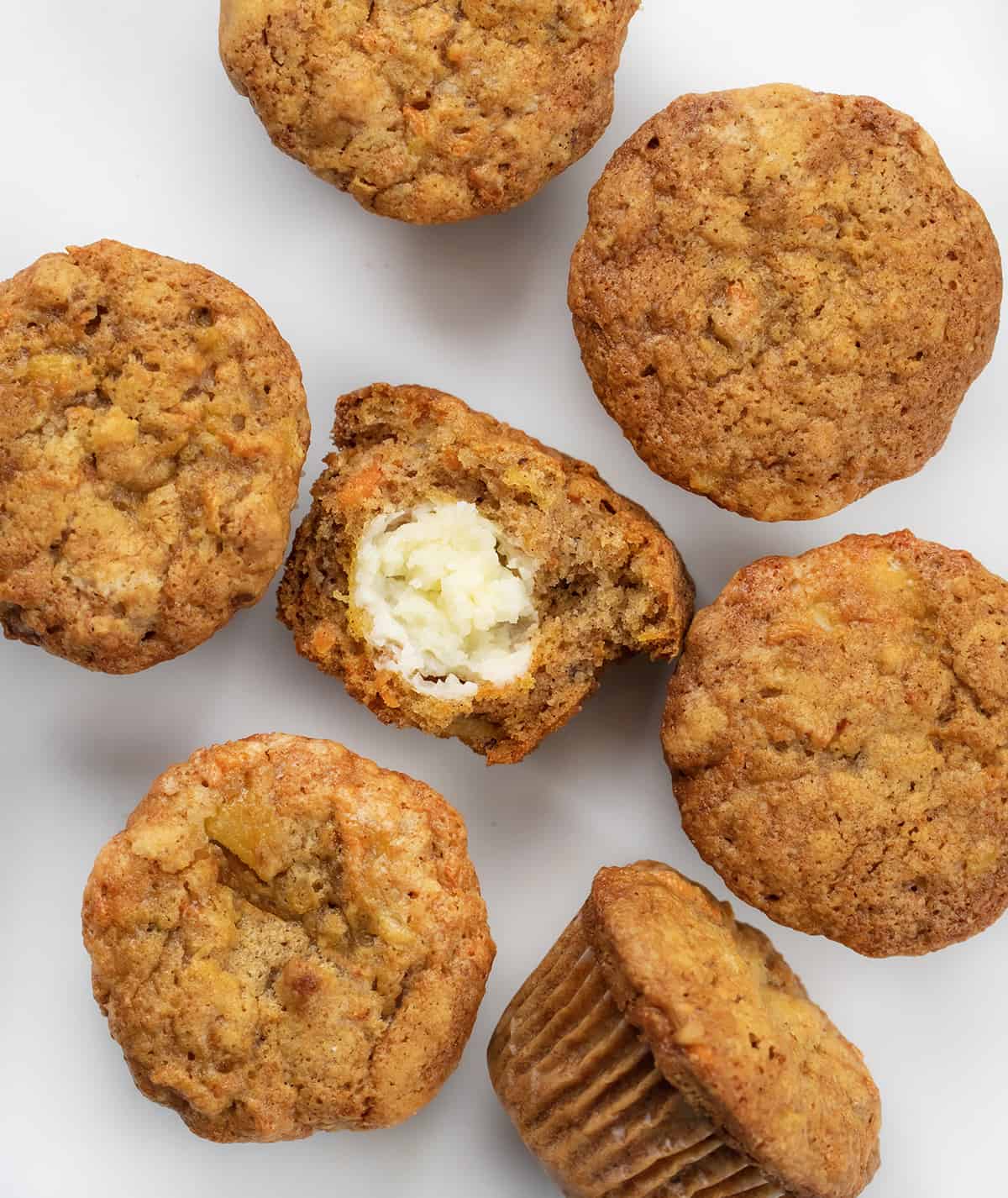 Cream Cheese-Filled Carrot Cake Cupcakes are rich and moist carrot cupcakes filled with a surprise cream cheese center! You still get the flavors of a cream cheese frosted carrot cake with each bite, but with the 'frosting' inside! Cream Cheese Filled Carrot Cake Cupcakes on a White Counter With One Halved Showing Cream Cheese Inside.