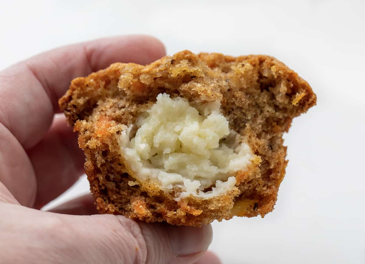 Cream Cheese-Filled Carrot Cake Cupcakes are rich and moist carrot cupcakes filled with a surprise cream cheese center! You still get the flavors of a cream cheese frosted carrot cake with each bite, but with the 'frosting' inside! Hand Holding Cream Cheese Filled Carrot Cake Cupcakes.