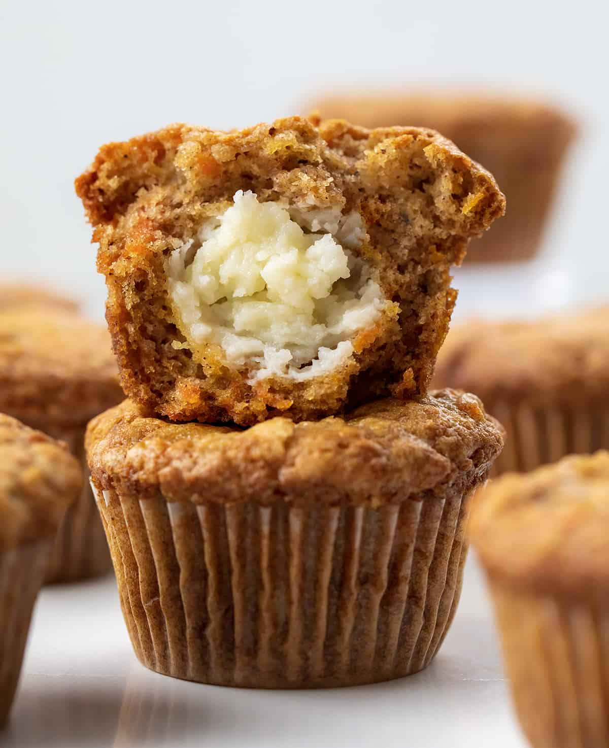 Cream Cheese-Filled Carrot Cake Cupcakes are rich and moist carrot cupcakes filled with a surprise cream cheese center! You still get the flavors of a cream cheese frosted carrot cake with each bite, but with the 'frosting' inside! Cream Cheese Filled Carrot Cake Cupcakes Stacked and Surrounded by More Cupcakes.