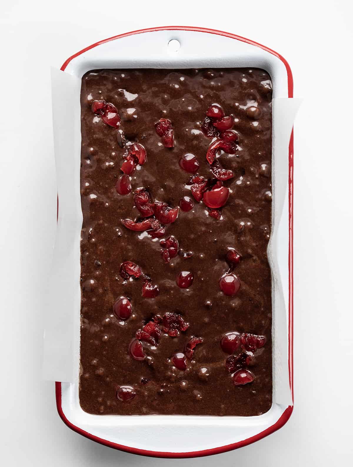 Cherry Brownie Bread is a dessert loaf of bread that merges the irresistible taste of a rich, chocolatey brownie with added cherries, baked, and topped with a cherry glaze. The cherries add a pop of bright flavor and a contrasting texture to the dense, chewy brownie bread. Whether you enjoy it as a sweet snack or as an after-dinner dessert, cherry brownie bread is sure to satisfy your cravings for something sweet and indulgent! Raw Cherry Brownie Bread Batter in a Pan Showing Cherries.