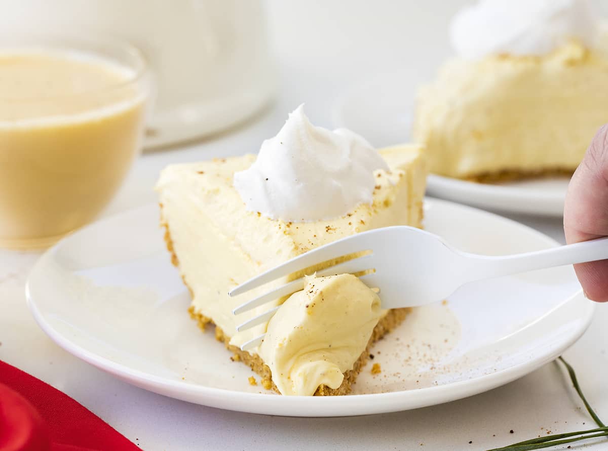 No-Bake Eggnog Pie is a creamy pie made with vanilla pudding mix, nutmeg, eggnog, rum, and whipped cream that tastes just like a glass of eggnog! Pie, No Bake Pie, Eggnog Pie, Leftover Eggnog Recipes, How to Use Eggnog, Graham Cracker Crust Pie, Dessert, Easy Pie, New Years Pie, i am baker, iambaker Slice of Eggnog Pie with Fork Removing a Bite