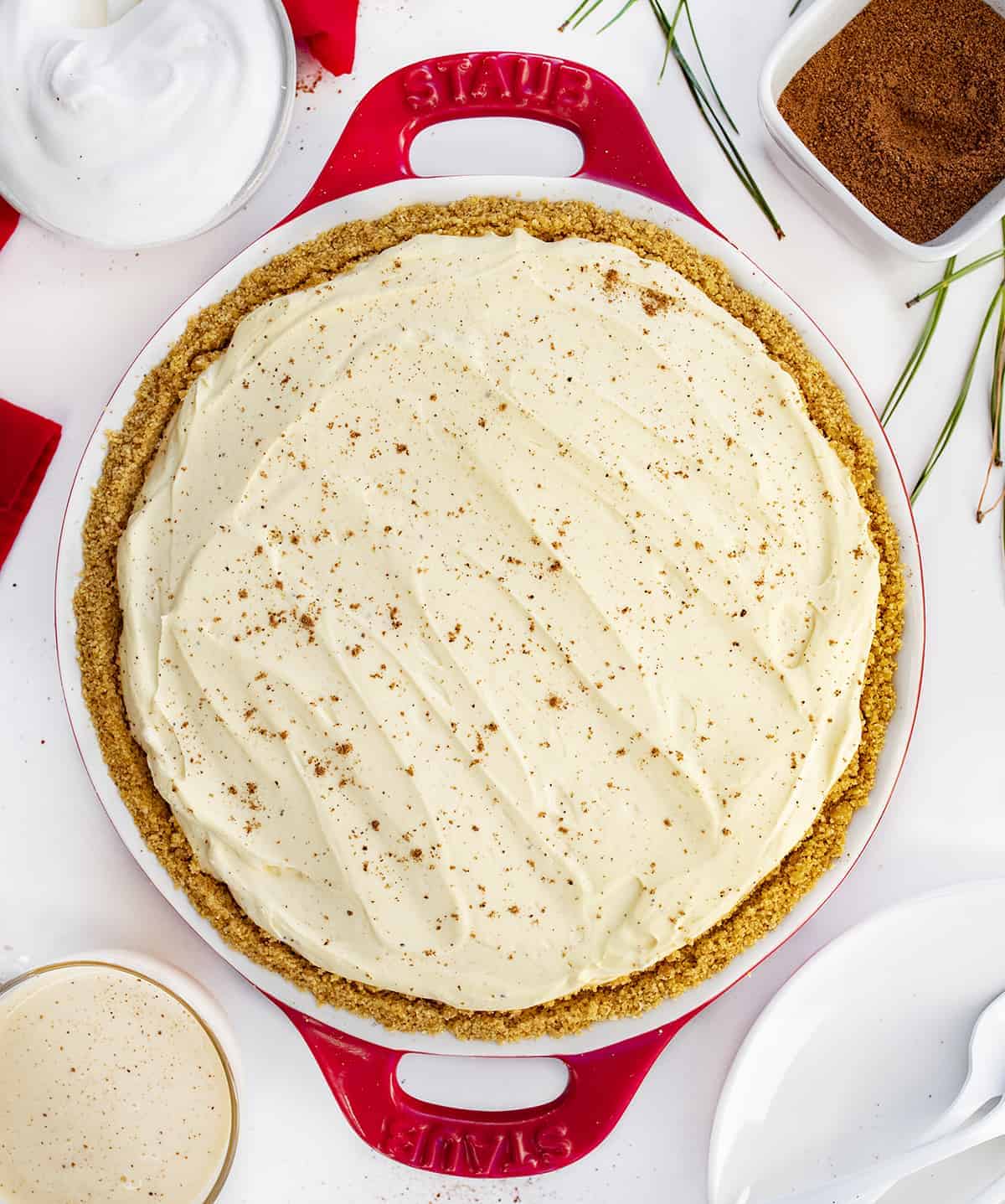 No-Bake Eggnog Pie is a creamy pie made with vanilla pudding mix, nutmeg, eggnog, rum, and whipped cream that tastes just like a glass of eggnog! Pie, No Bake Pie, Eggnog Pie, Leftover Eggnog Recipes, How to Use Eggnog, Graham Cracker Crust Pie, Dessert, Easy Pie, New Years Pie, i am baker, iambaker Whole Eggnog Pie in Red Pie Dish