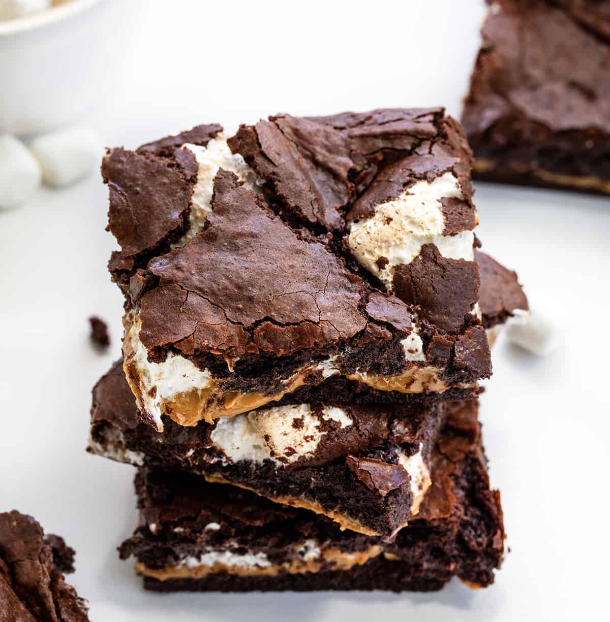 Fluffernutter Brownies are creamy peanut butter and marshmallow fluff sandwiched and baked between two layers of the ultimate fudgy brownies. The brownie layers provide a rich, chocolaty flavor, while the peanut butter and marshmallow layers add a creamy and fluffy contrast! Stack of Fluffernutter Brownies on a White Counter.