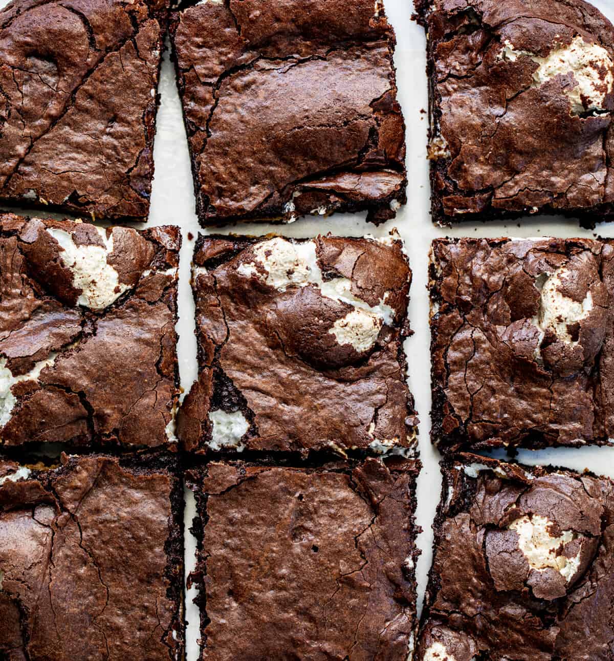 Fluffernutter Brownies are creamy peanut butter and marshmallow fluff sandwiched and baked between two layers of the ultimate fudgy brownies. The brownie layers provide a rich, chocolaty flavor, while the peanut butter and marshmallow layers add a creamy and fluffy contrast! Fluffernutter Brownies From Above Right Out of the Oven and Cut Into Squares.