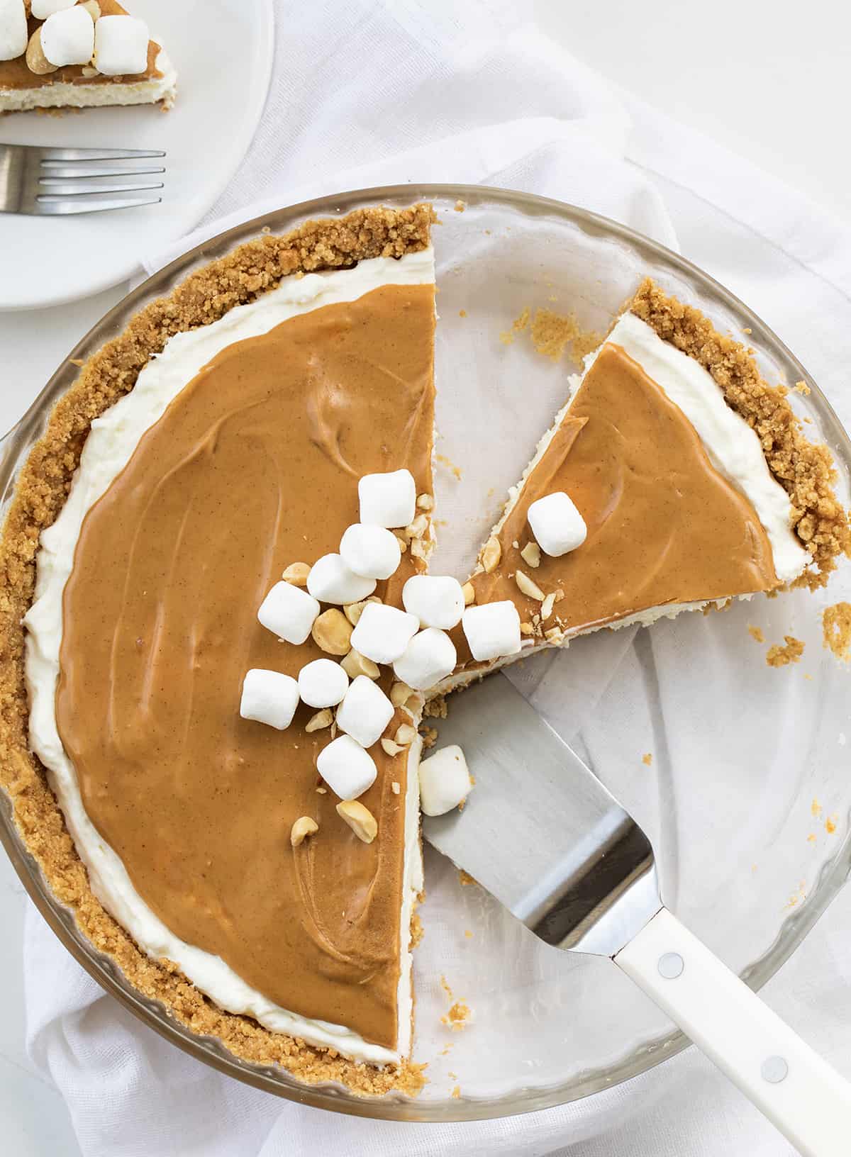 Fluffernutter Pie is a no-bake dessert made with a soft and smooth marshmallow filling topped with creamy peanut butter, all in a graham cracker crust. It's another delightful addition to my list of fluffernutter treats that started with my Fluffernutter Cookies! Cut Into Fluffernutter Pie with Three Pieces Removed and One Left in the Pie Plate and a Spatula.