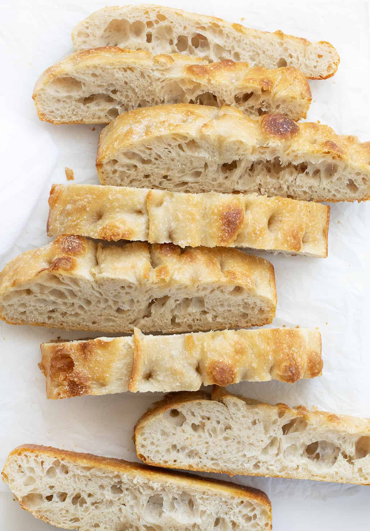 Sourdough Focaccia is fluffy and chewy on the inside with a crispy outside, made with an active sourdough starter for that sourdough flavor in every bite! It is delicious on its own, but also pairs wonderfully with various spreads and dipping options. Plus, it is made in a baking dish with just a few ingredients and no yeast. If you have a little patience, you can certainly make this bread. Cut up Pieces of Sourdough Focaccia on a White Cutting Board.