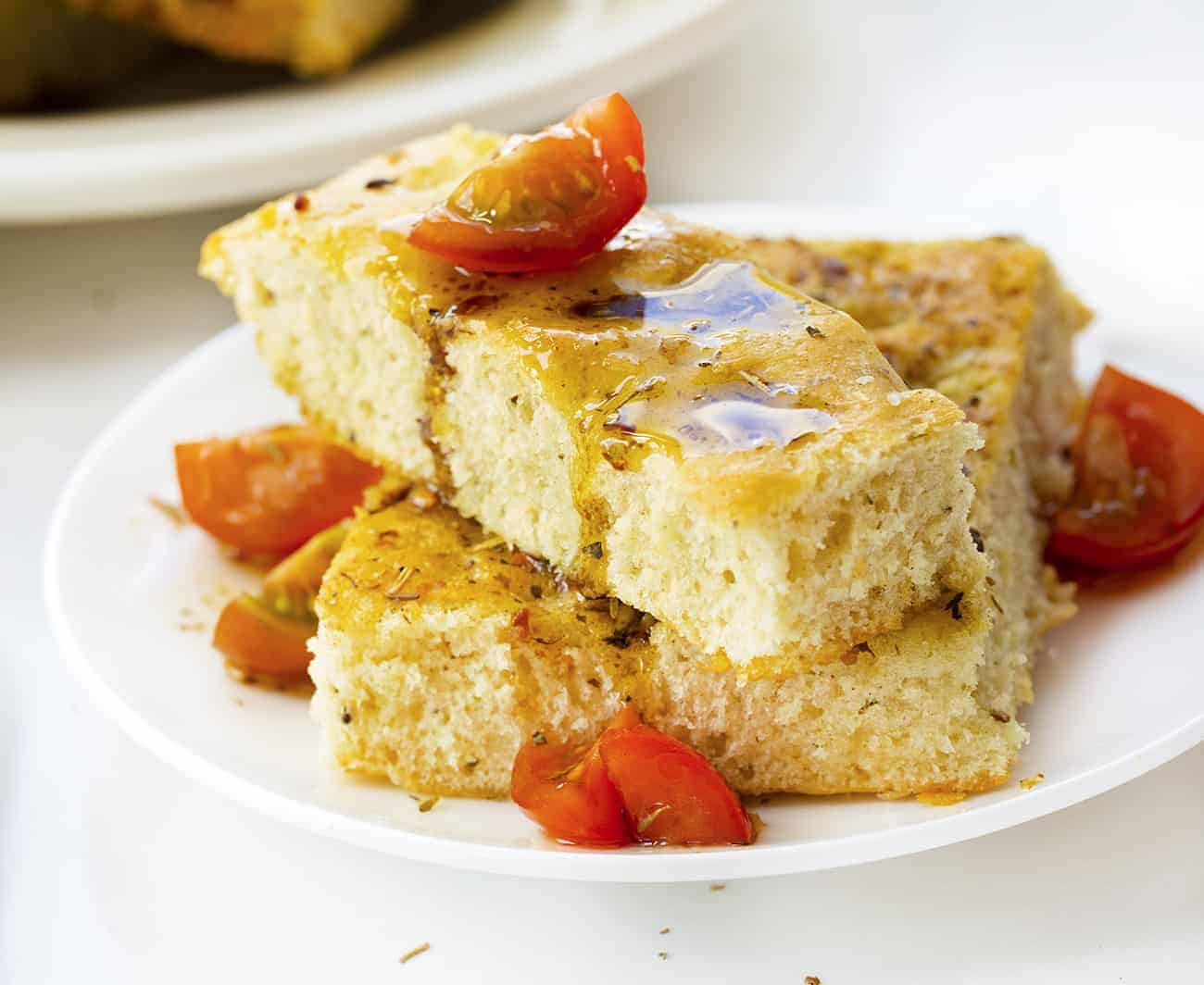 Focaccia Bread is an Italian bread that is made with lots of olive oil and full of Italian seasoning for a delicious and savory snack or appetizer. focaccia bread, bread recipes, Italian bread, i am baker, iambaker, homemade focaccia bread recipe, baking bread Focaccia Bread that has been Drizzled with Oil and Balsamic Vinegar on a White Plate with Tomato
