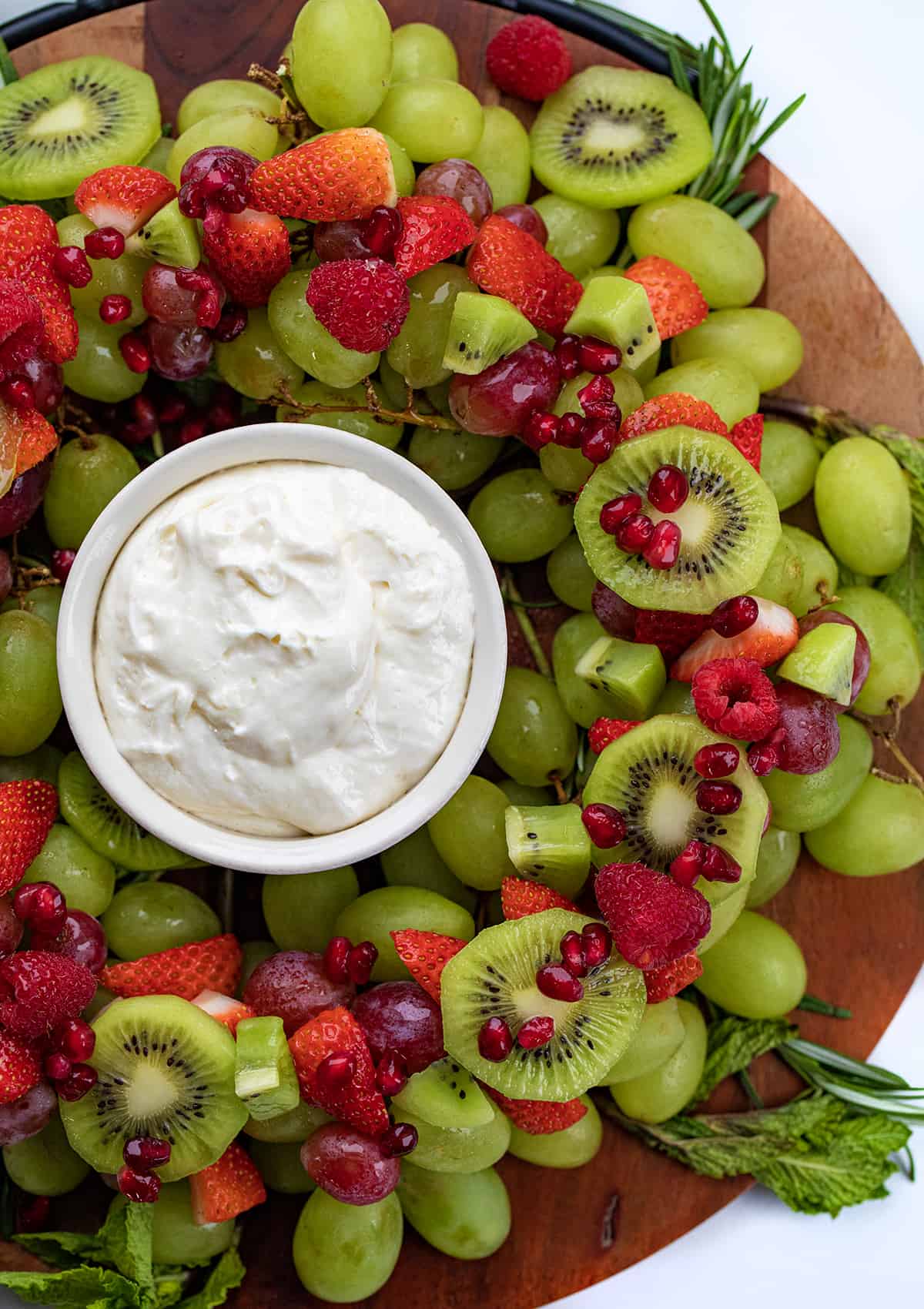 Holiday Wreath Fruit Tray is a beautiful and colorful display of fruit and herbs in a circular design with fruit dip in the center for serving. The fruit tray is presented to represent a wreath, a popular symbol of Christmas. Be sure to add this to your holiday menu! Close up of Holiday Wreath Fruit Tray with Red and Green Fruit and Fruit Dip.