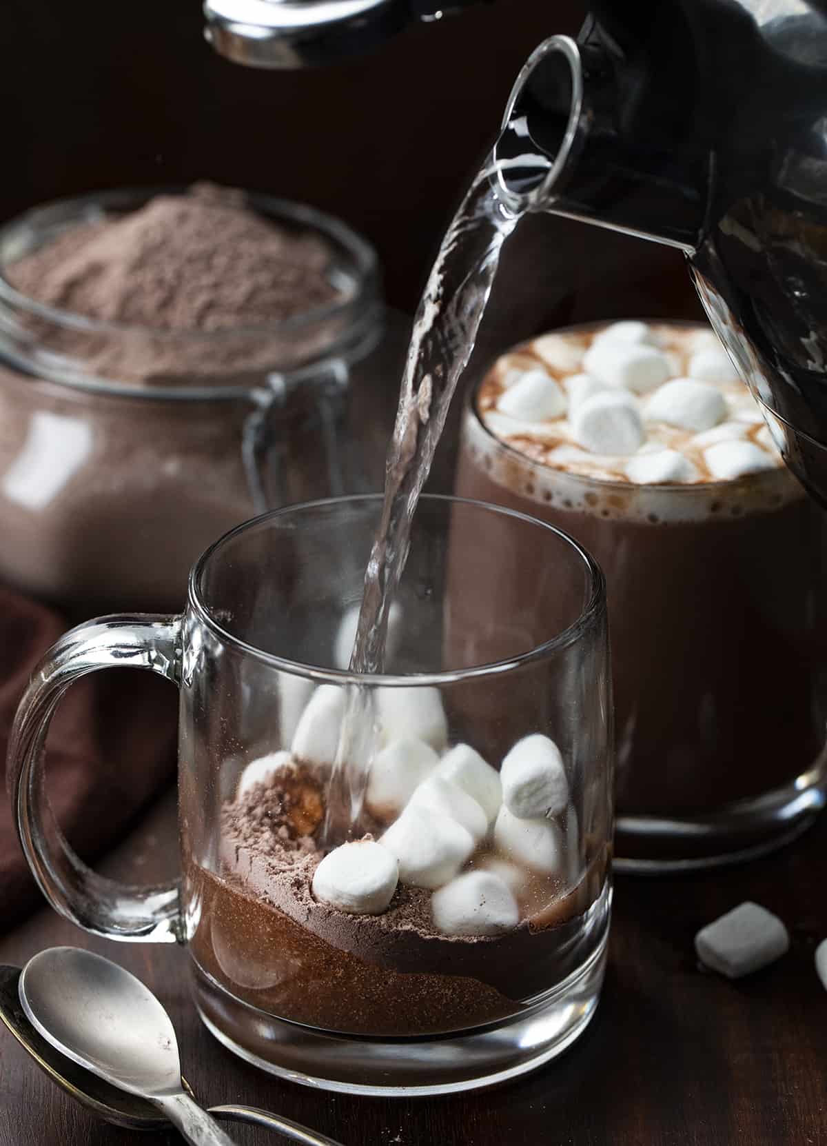 Homemade Hot Cocoa Mix is cheaper than store-bought and tastes so much better! Nothing warms a body up like a mug of rich hot cocoa, especially in the winter. And, it's a beverage that can be enjoyed by all ages. I love that you know exactly what is going into the powdery mix with no added preservatives. This hot chocolate recipe is rich, velvety, decadent, and the perfect beverage for a crowd! Pouring hot water to a glass with homemade hot cocoa mix and mini marshmallows in it.