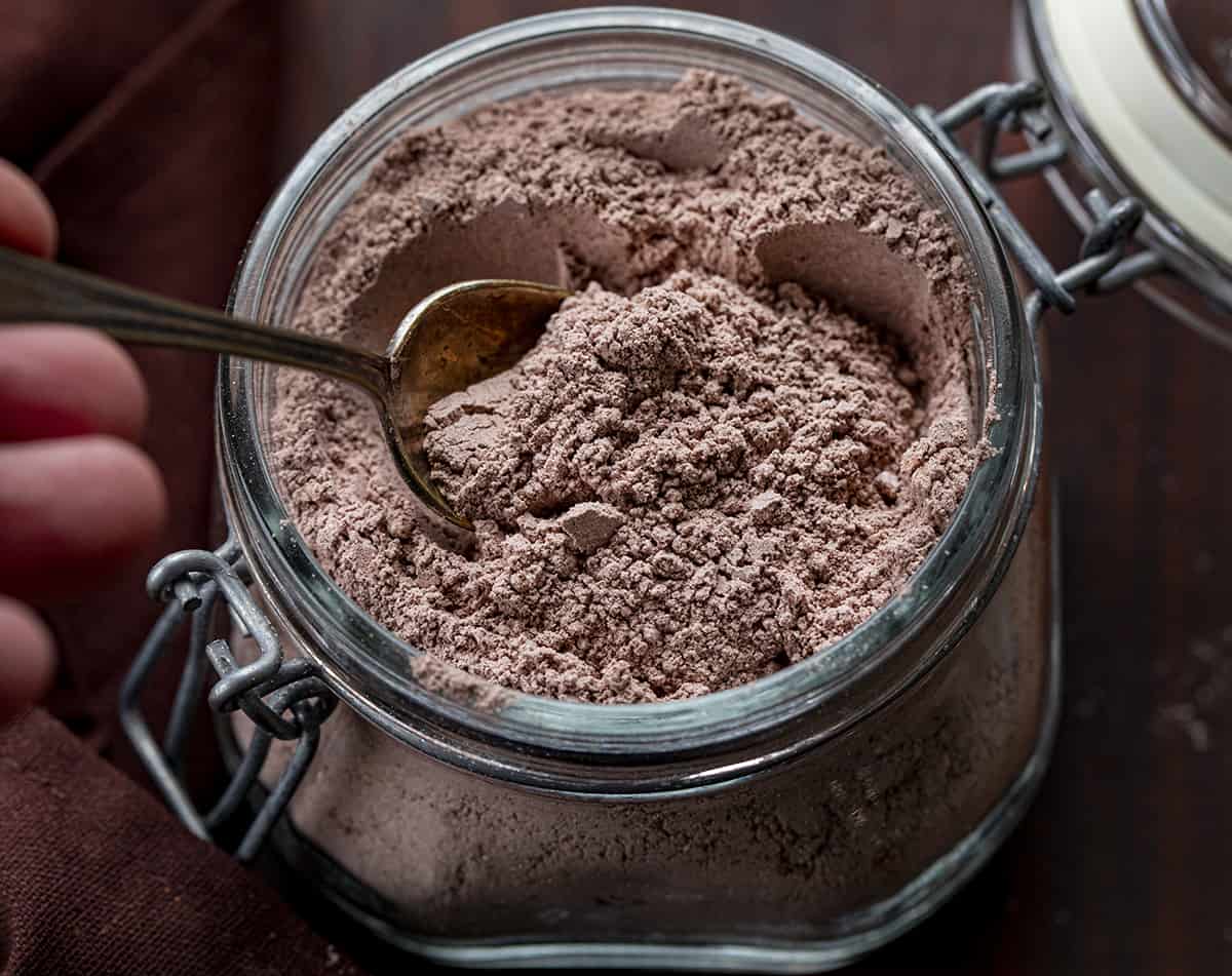 Homemade Hot Cocoa Mix is cheaper than store-bought and tastes so much better! Nothing warms a body up like a mug of rich hot cocoa, especially in the winter. And, it's a beverage that can be enjoyed by all ages. I love that you know exactly what is going into the powdery mix with no added preservatives. This hot chocolate recipe is rich, velvety, decadent, and the perfect beverage for a crowd! Spoon in a jar of homemade hot cocoa mix on a cutting board.