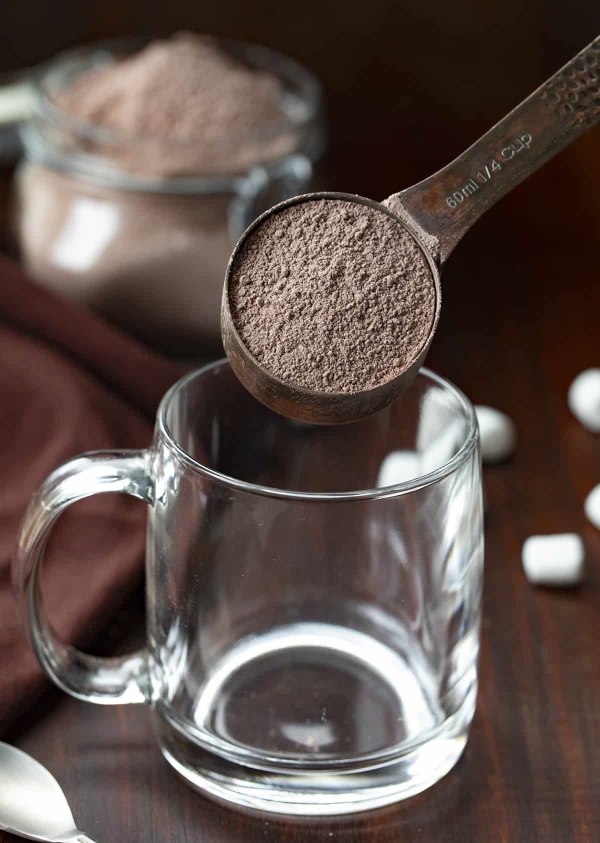 Homemade Hot Cocoa Mix is cheaper than store-bought and tastes so much better! Nothing warms a body up like a mug of rich hot cocoa, especially in the winter. And, it's a beverage that can be enjoyed by all ages. I love that you know exactly what is going into the powdery mix with no added preservatives. This hot chocolate recipe is rich, velvety, decadent, and the perfect beverage for a crowd! A 1/4 cup measuring scoop adding hot cocoa mix to an empty glass.