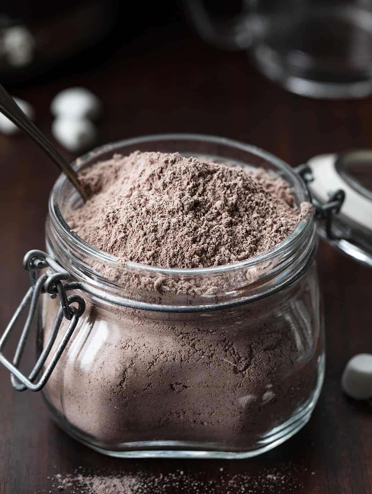 Homemade Hot Cocoa Mix is cheaper than store-bought and tastes so much better! Nothing warms a body up like a mug of rich hot cocoa, especially in the winter. And, it's a beverage that can be enjoyed by all ages. I love that you know exactly what is going into the powdery mix with no added preservatives. This hot chocolate recipe is rich, velvety, decadent, and the perfect beverage for a crowd! Jar of homemade hot cocoa mix open and with a spoon in it.