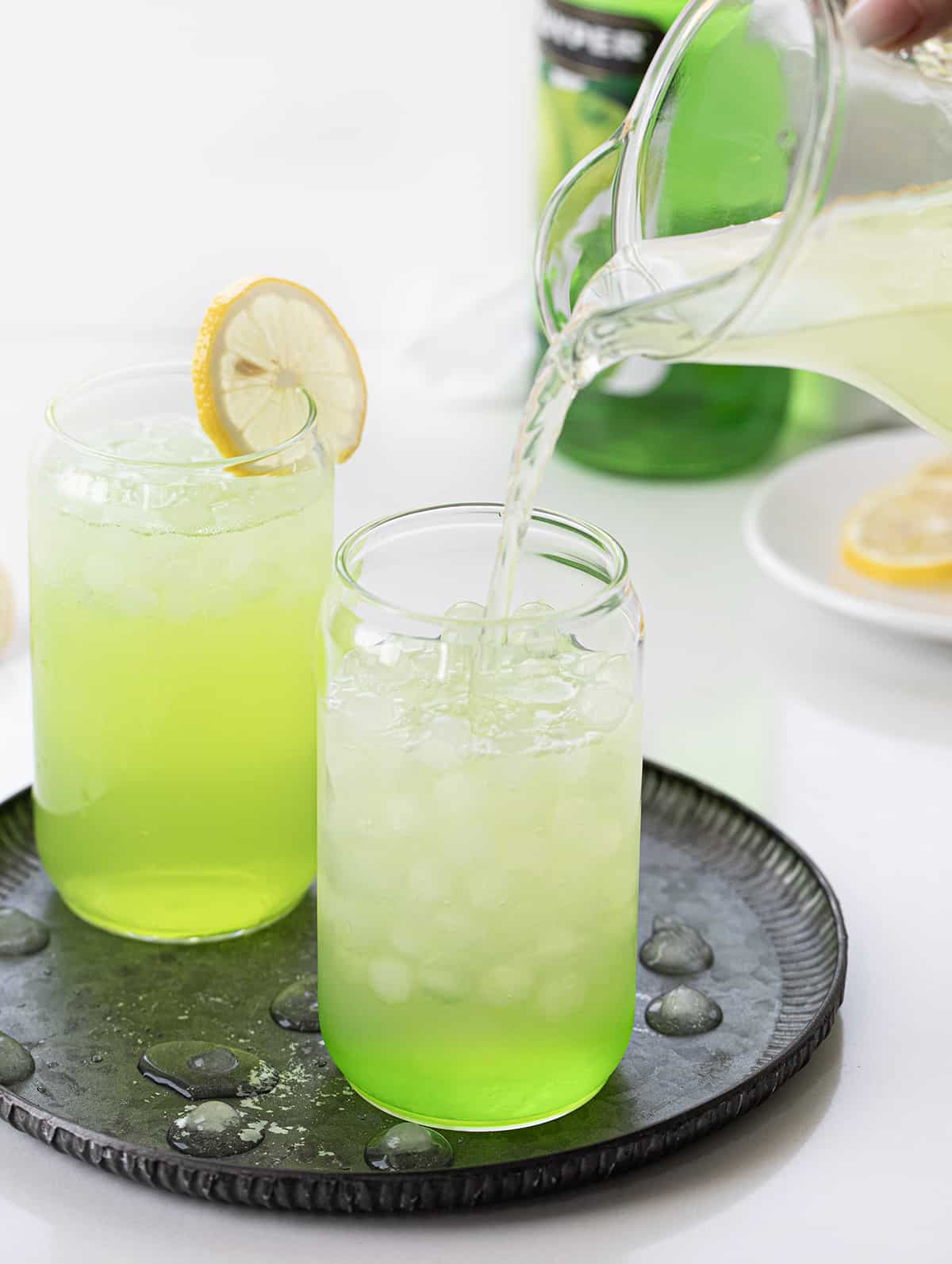 Hulk Smash is an alcoholic beverage made with Midori, sour apple liqueur, and lemonade, all poured over lemonade ice cubes. Both the name and the green color of the drink will remind you of the fictional character 'The Hulk' from Marvel Comics! But don't worry, you won't turn into the Hulk after drinking one, but the sweet drink does pack a punch (pun intended)! Adding Lemonade to Glass to Make Hulk Smash Cocktail.