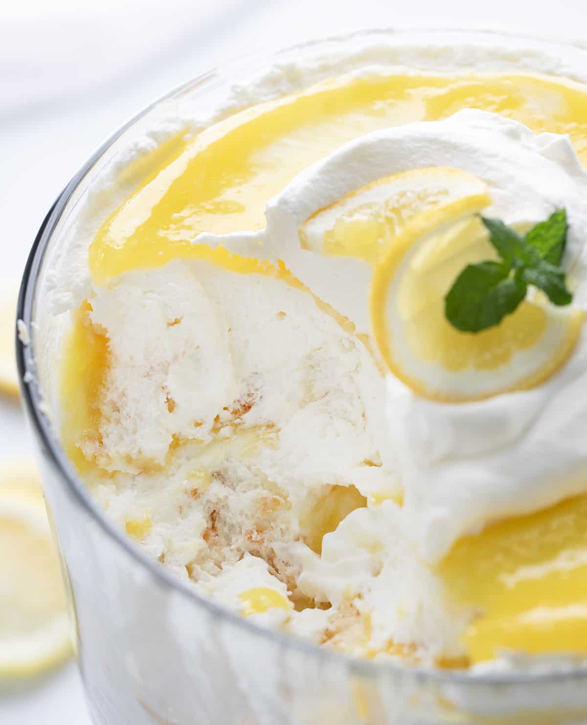 Lemon Cream Trifle is a layered dessert made with cubes of angel food cake, whipped cream, and homemade lemon curd. Each refreshing and indulgent bite is full of lemon flavor with a lovely blend of textures. If you love lemon desserts, you will definitely want to keep the lemon curd recipe on hand for more desserts and treats! Lemon Cream Trifle with some Removed Showing the Gooey Texture inside.