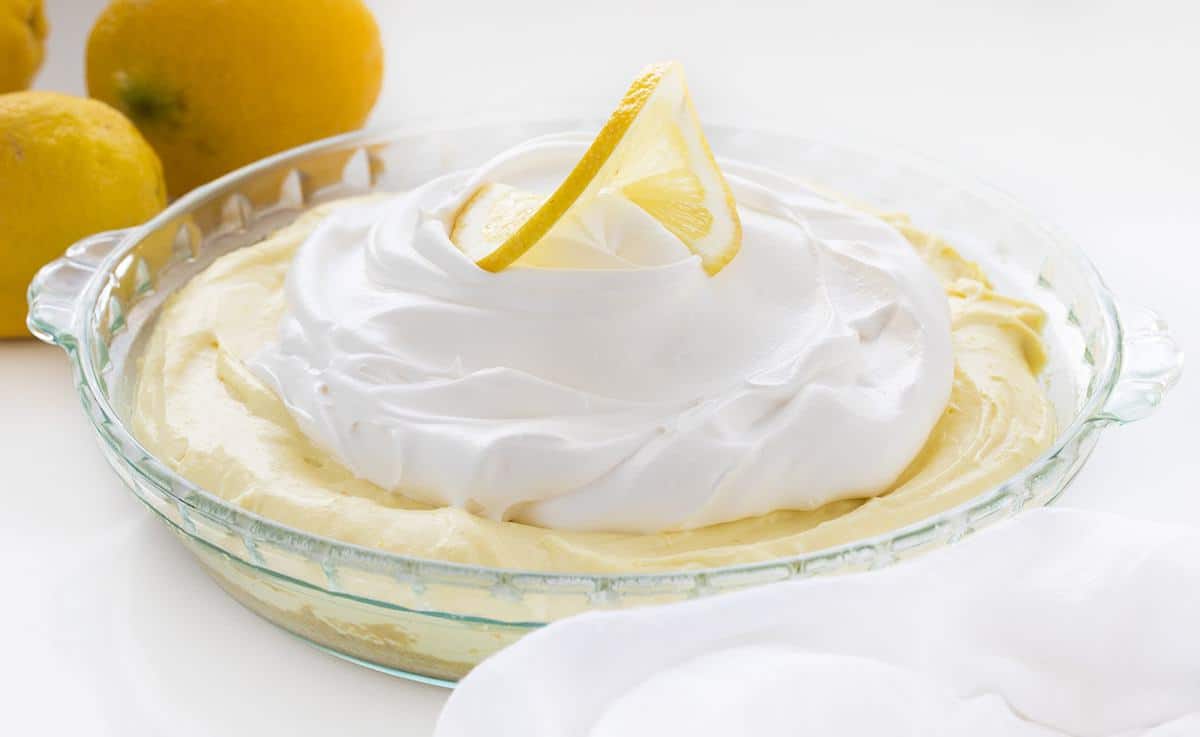 Lemonade Pie is a no-bake dessert that is as delicious and refreshing as a tall glass of lemonade on a hot summer day. iambaker, lemonade pie, no-bake desserts, summer desserts, lemonade, pie recipes, i am baker, cream pie, recipes, dessert One Lemonade Pie in Glass Pie Pan with Lemons Behind It