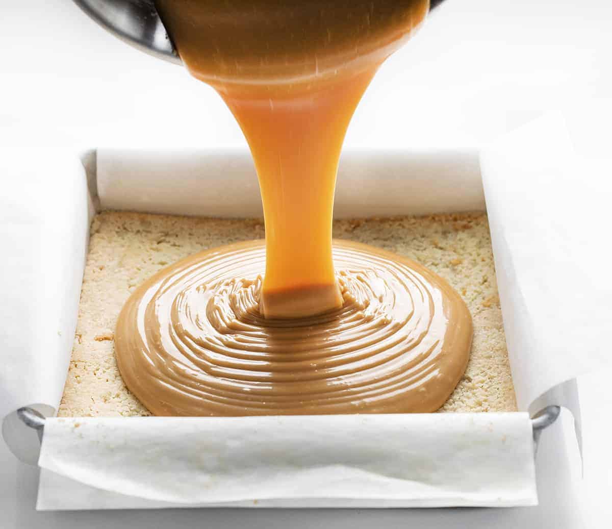 Millionaire's Bars are a sweet, layered dessert made with a shortbread crust, caramel filling, and a semi-sweet chocolate topping. Millionaire Bars, How to Make Millionaire Bars, The Best Millionaire Bars, Billionaire Bars, Bars, Dessert, Recipes, Chocolate, Caramel, Soft Caramel, i am baker, iambaker Pouring Caramel onto Shortbread for Millionaire Bars