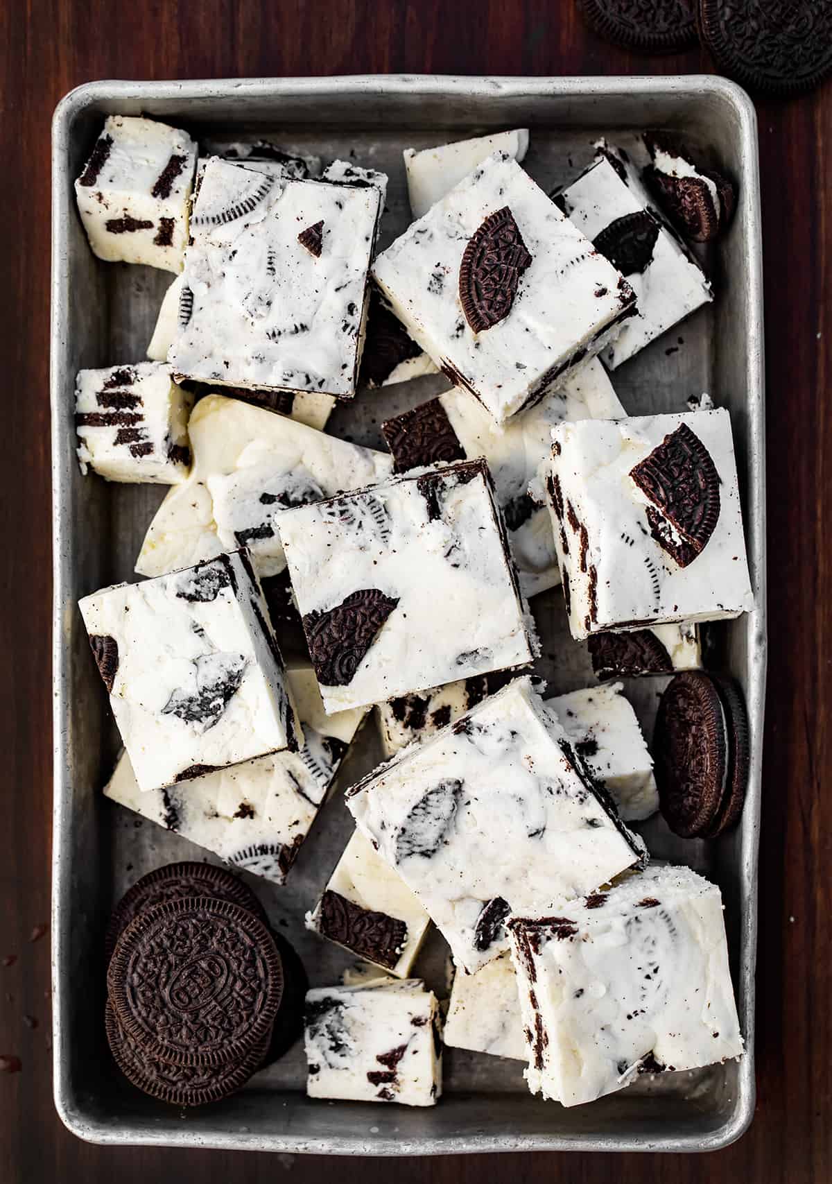 Cookies and Cream Fudge is an easy-to-make treat with white chocolate chips, marshmallow fluff, and Oreo cookies. It should definitely be added to your list of holiday treats this season! Pan of Cookies and Cream Fudge Cut Into Pieces with Some Oreos Near the Fudge.