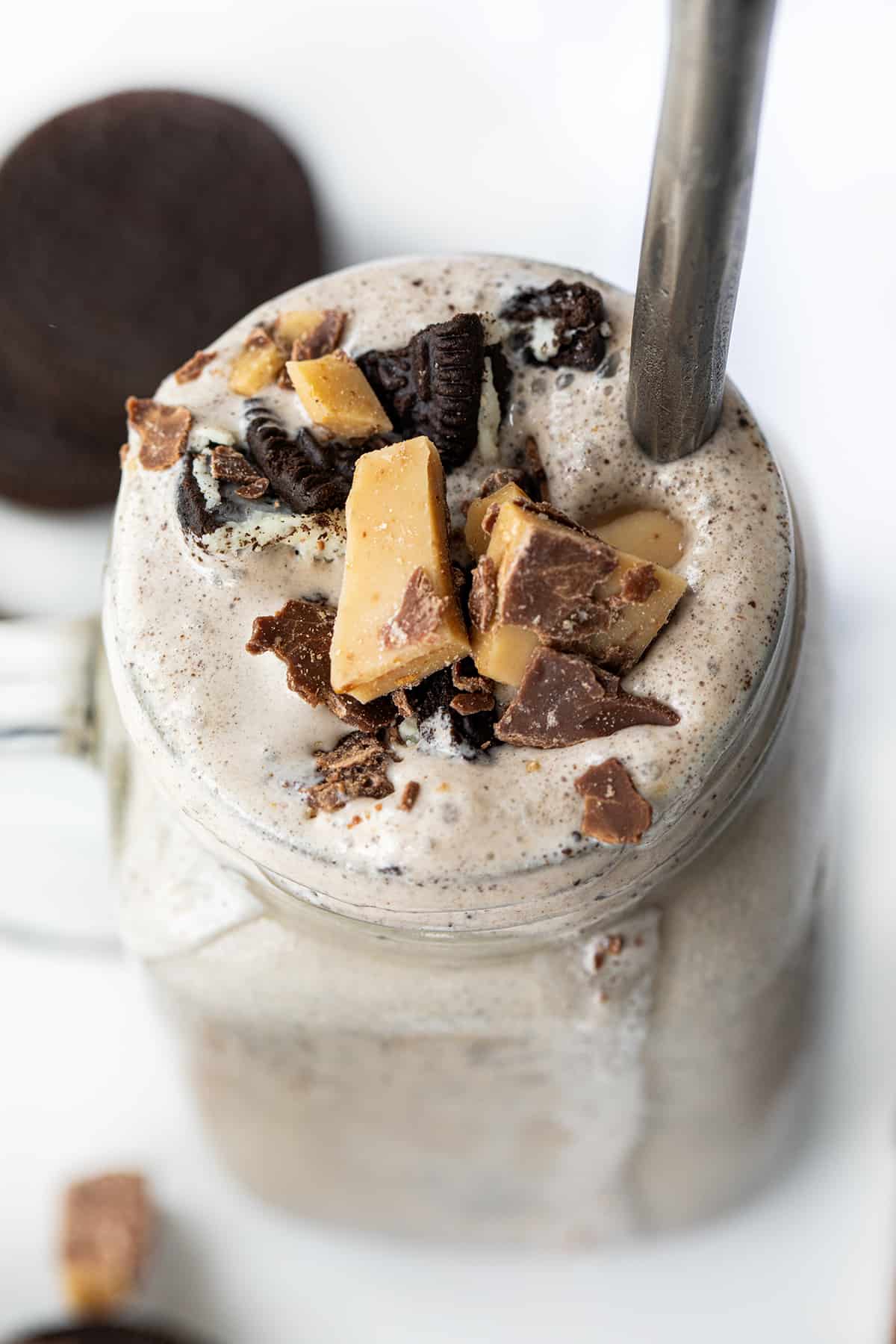 Oreo Heath Blizzard is a frozen dessert that combines the beloved taste of Oreo cookies with the rich, buttery sweetness of a Heath candy bar. This flavor combination is my favorite way to order a Blizzard at Dairy Queen, although when you order it you do have to specify "no added hot fudge". I love it so much I decided to create a recipe for it at home, and it does not disappoint! Easy, will satisfy your sweet tooth, and cool you down on a hot day! Mug of Oreo Heath Blizzard, a Recipe Adaptation Based on Dairy Queens Blizzard, and Surrounded by Oreos and Heath.