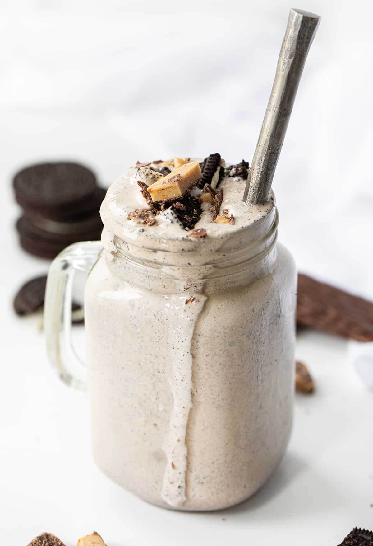 Oreo Heath Blizzard is a frozen dessert that combines the beloved taste of Oreo cookies with the rich, buttery sweetness of a Heath candy bar. This flavor combination is my favorite way to order a Blizzard at Dairy Queen, although when you order it you do have to specify "no added hot fudge". I love it so much I decided to create a recipe for it at home, and it does not disappoint! Easy, will satisfy your sweet tooth, and cool you down on a hot day! Mug of Oreo Heath Blizzard, a Recipe Adaptation Based on Dairy Queens Blizzard, and Surrounded by Oreos and Heath.
