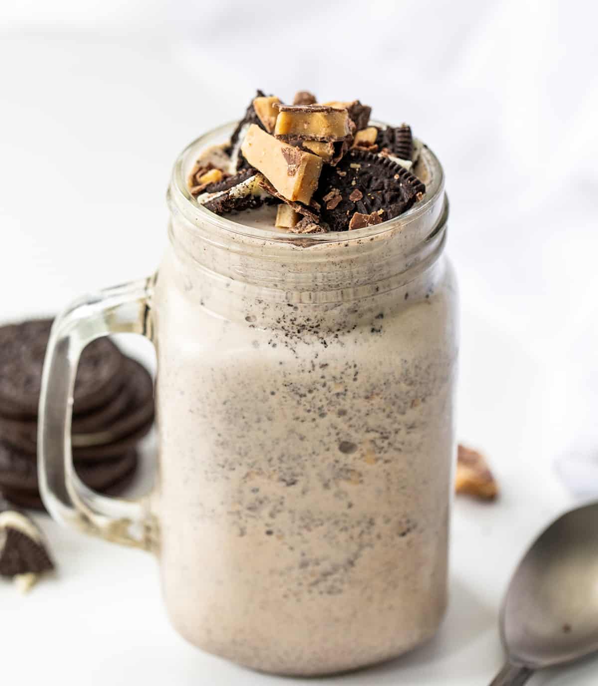 Oreo Heath Blizzard is a frozen dessert that combines the beloved taste of Oreo cookies with the rich, buttery sweetness of a Heath candy bar. This flavor combination is my favorite way to order a Blizzard at Dairy Queen, although when you order it you do have to specify "no added hot fudge". I love it so much I decided to create a recipe for it at home, and it does not disappoint! Easy, will satisfy your sweet tooth, and cool you down on a hot day! Mug of Oreo Heath Blizzard, a Recipe Adaptation Based on Dairy Queens Blizzard, and Surrounded by Oreos and Heath.