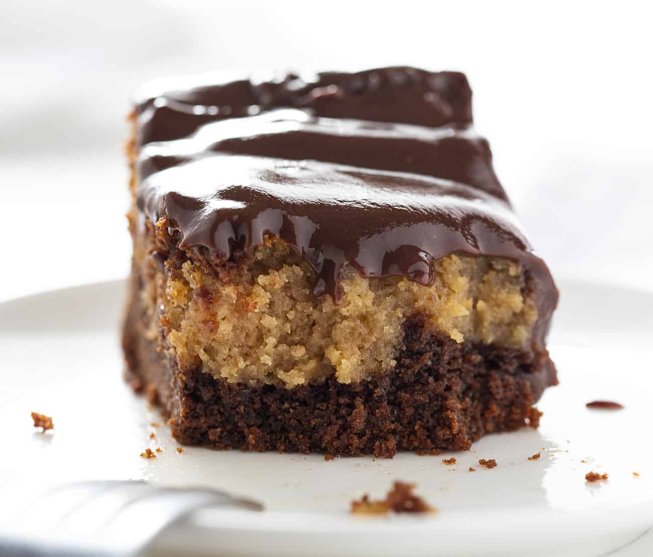 Chocolate Peanut Butter Ooey Gooey Cake takes my Chocolate Ooey Gooey Cake to a new level--a peanut butter level! chocolate peanut butter ooey gooey cake, chocolate ooey gooey cake, ooey gooey butter cake, chocolate peanut butter cake, chocolate cake, how to bake chocolate peanut butter ooey gooey cake, chocolate peanut butter ganache, ganache, dessert recipes, baking, i am baker Chocolate Peanut Butter Ooey Gooey Cake with Fork Resting on White Plate