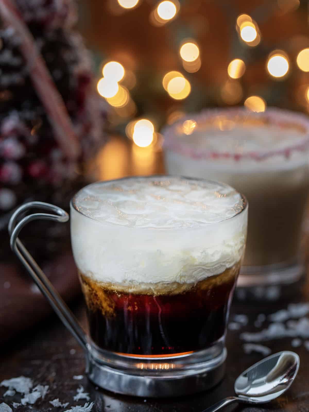 This alcoholic beverage gives a peppermint and festive twist to a White Russian cocktail. It still contains Kahlua, vodka, and cream. But then has added peppermint schnapps to give it a minty twist. And, don't forget about the crushed candy cane around the rim of the glass. That will really be a lovely touch if serving at your Christmas or New Year's Eve parties. Peppermint White Russians in front of a Christmas Tree and Twinkling Lights.
