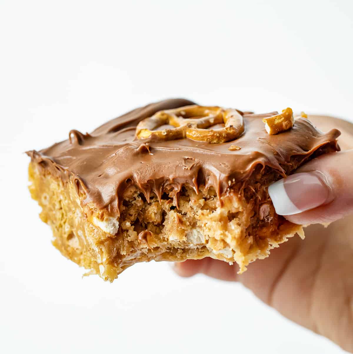 Pretzel Scotcheroos are delightful, no-bake dessert bars that combine sweet, salty, and crunchy flavors and textures. You get the sweetness of the syrup mixture, the richness of peanut butter, the crunchiness of pretzels and cereal, and the smoothness of chocolate and butterscotch. Each bite will surely satisfy both your sweet and salty cravings! Hand Holding a Bit Into Pretzel Scotcheroo.