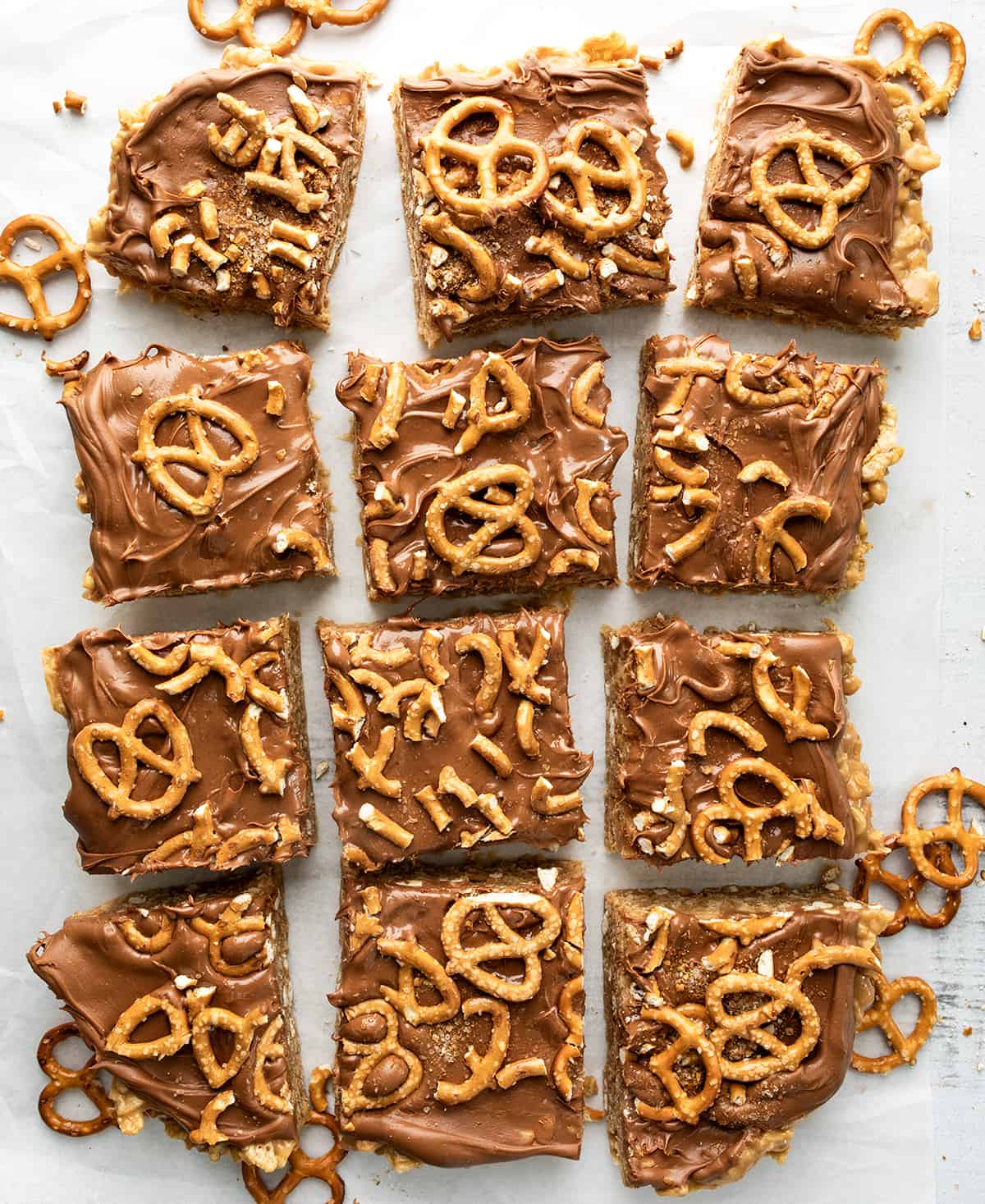 Pretzel Scotcheroos are delightful, no-bake dessert bars that combine sweet, salty, and crunchy flavors and textures. You get the sweetness of the syrup mixture, the richness of peanut butter, the crunchiness of pretzels and cereal, and the smoothness of chocolate and butterscotch. Each bite will surely satisfy both your sweet and salty cravings! Pretzel Scotcheroo Bars from Overhead on a White Counter with a few Pretzels Around.