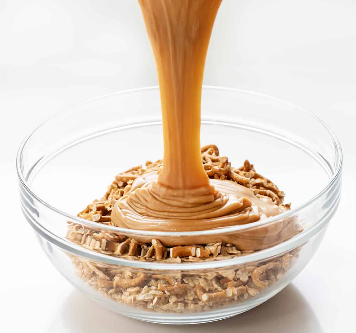 Pretzel Scotcheroos are delightful, no-bake dessert bars that combine sweet, salty, and crunchy flavors and textures. You get the sweetness of the syrup mixture, the richness of peanut butter, the crunchiness of pretzels and cereal, and the smoothness of chocolate and butterscotch. Each bite will surely satisfy both your sweet and salty cravings! Adding Caramel Mixture to Pretzel Scotcheroos Bowl of Ingredients.