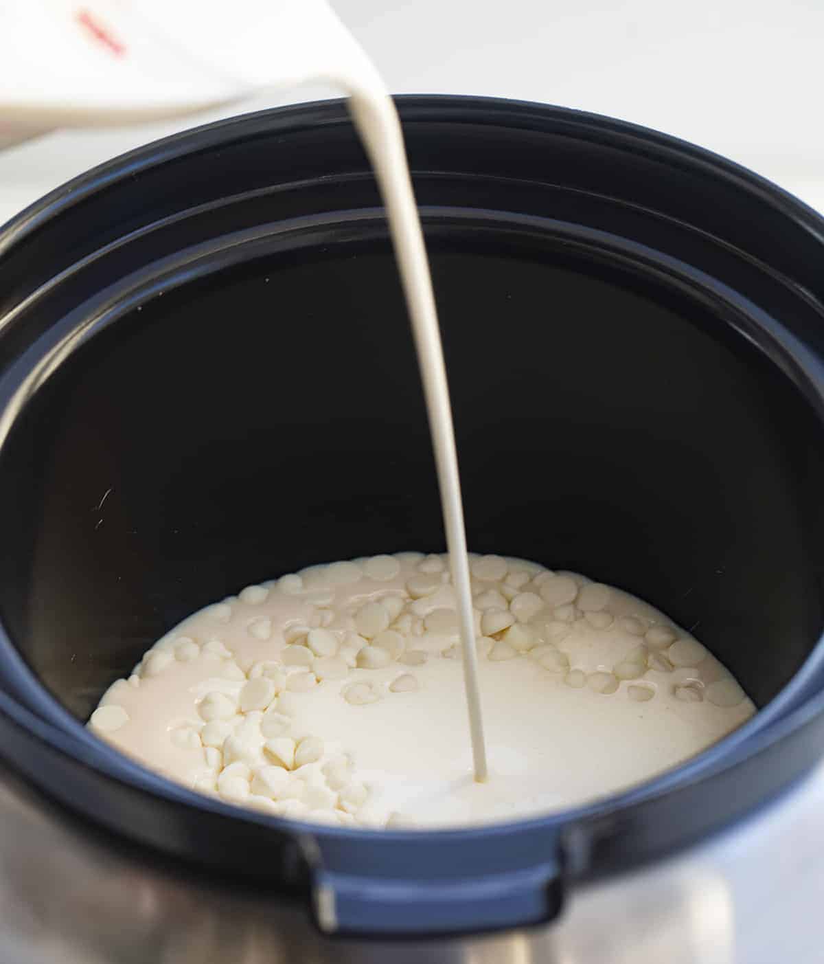 Snowed-in White Hot Chocolate Cocktail is an adult beverage made in a slow cooker with white chocolate, whipping cream, milk, vanilla, and RumChata. Hot Chocolate, Hot Cocoa, Boozy Hot Cocoa, Adult Hot Chocolate, White Chocolate Hot Chocolate, Rumchata Hot Cocoa, beverages, drinks, boozy drinks, winter drinks, i am baker, iambaker Adding Ingredients to White Chocolate Hot Cocoa